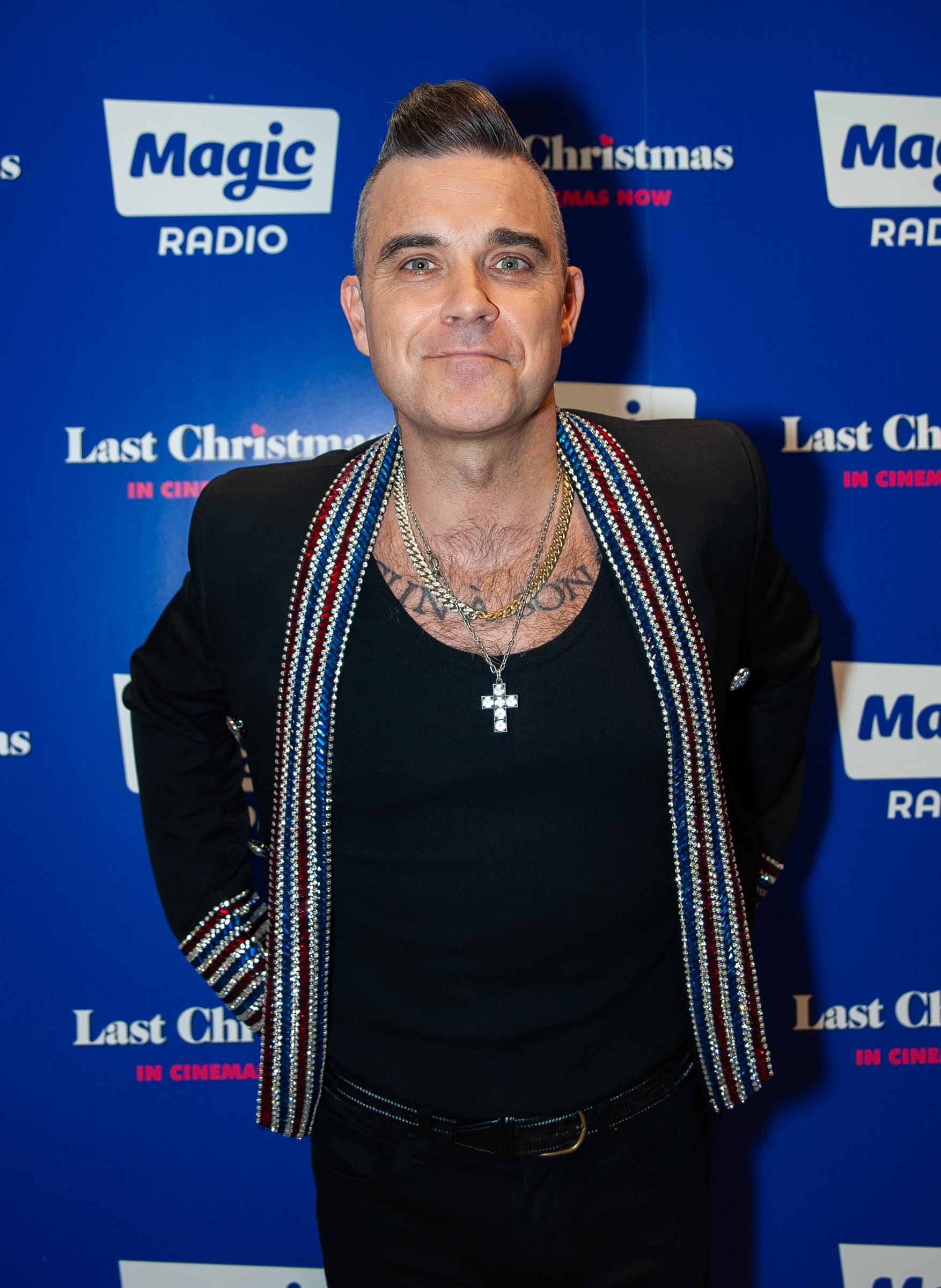 Robbie Williams attended Magic Radio's Magic of Christmas with "Last Christmas" on November 24, 2019, in London, England. Wearing a glitter-trimmed jacket and layered chains, he struck a confident pose, bringing his signature charm to the festive event.
