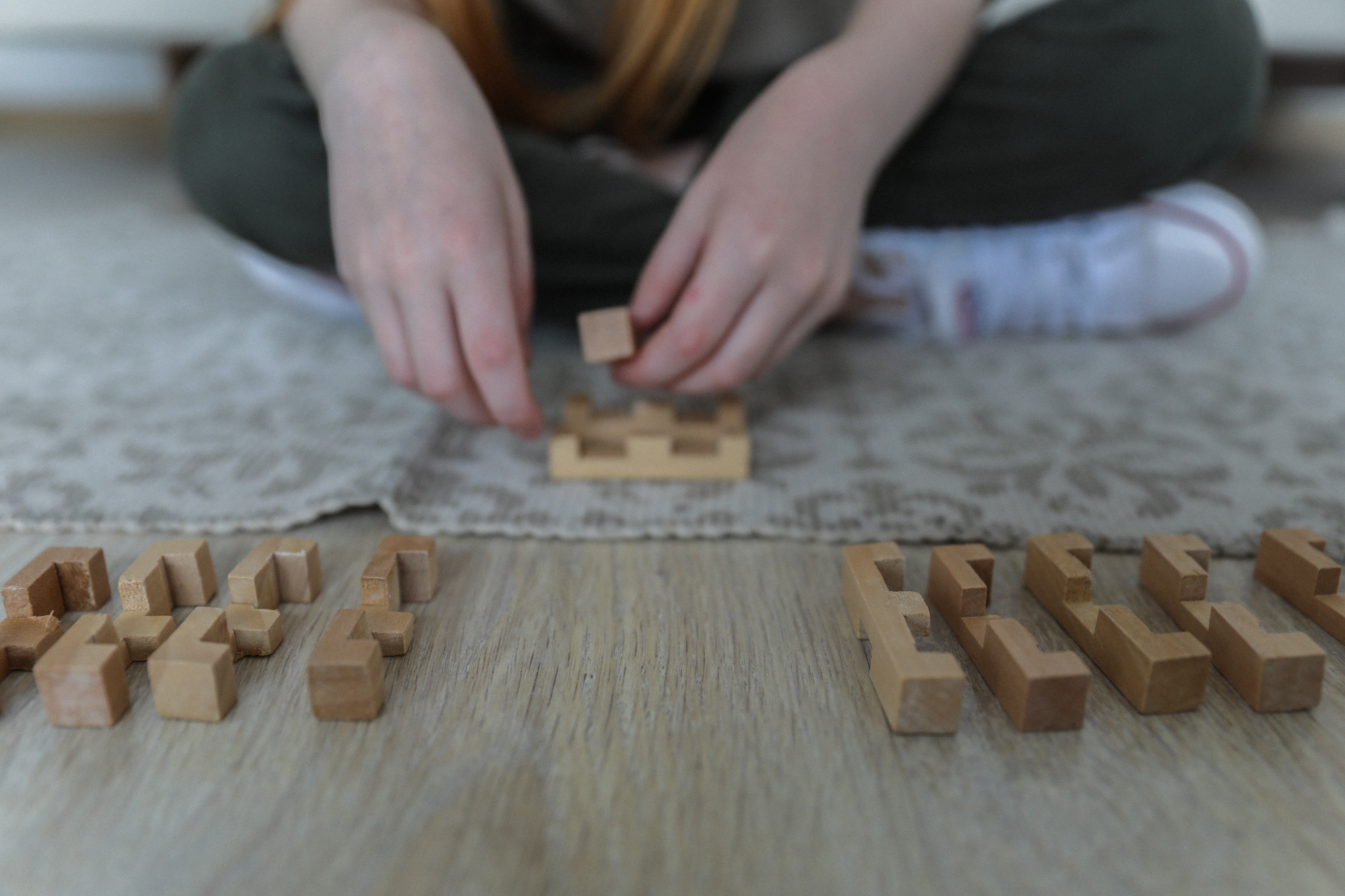 A girl attempts to make sense of wooden puzzle blocks laid out in front of her | Photo: Pexels/Monstera 