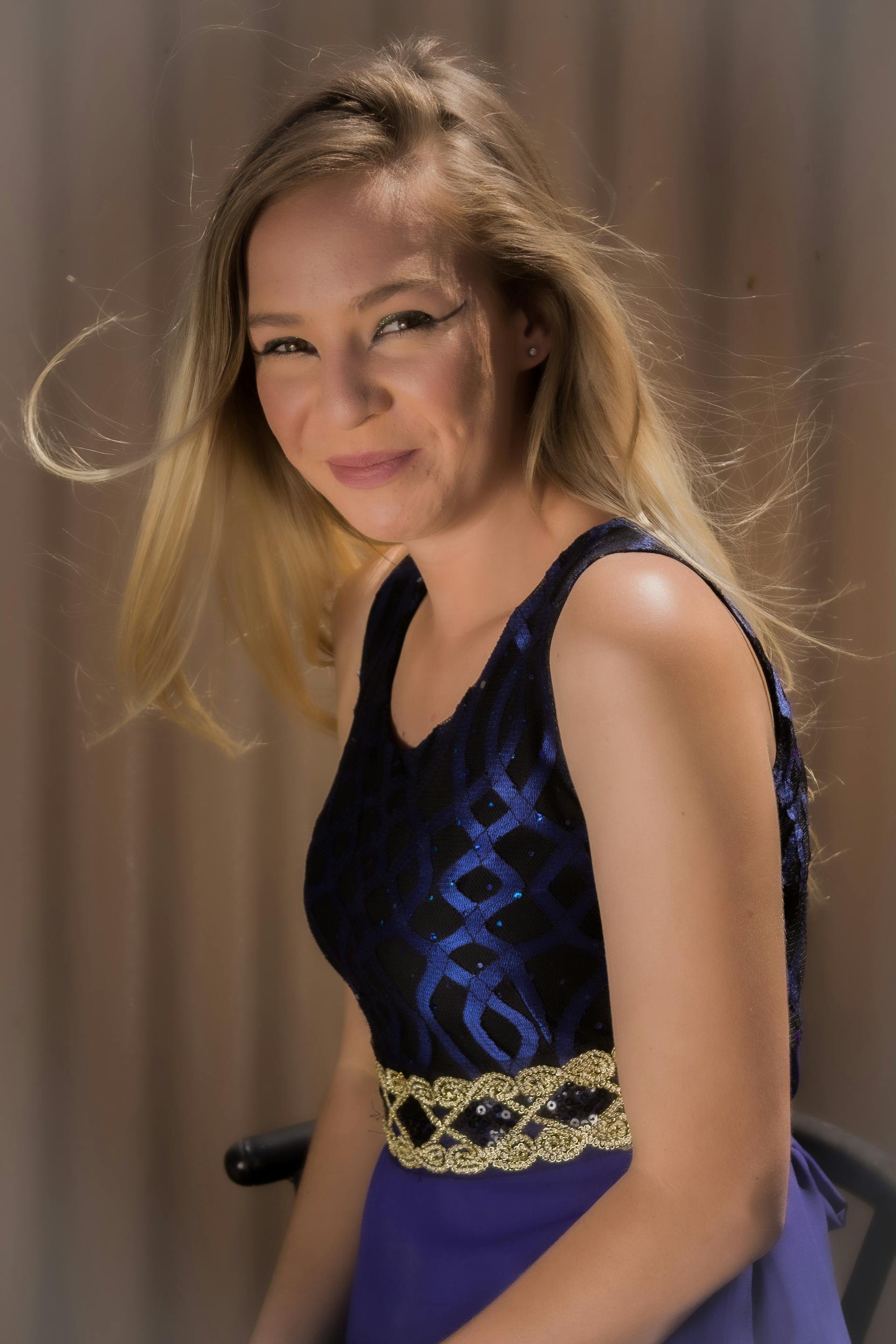 Una hermosa joven rubia sonriendo mientras luce un vestido azul y dorado brillante | Fuente: Pexels