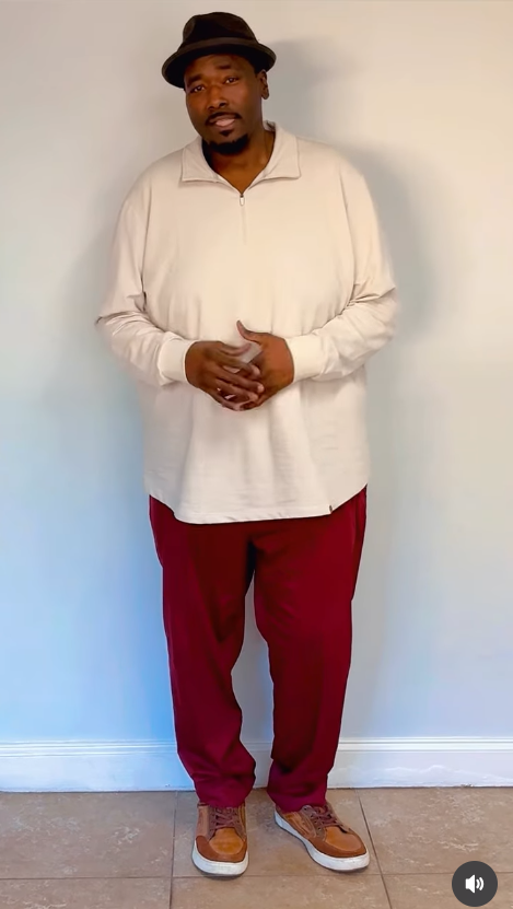 Quinton Aaron in a video wears a brown fedora and a loose cream long-sleeve shirt and bright red pants. | Source: Instagram/officialquintonaaron