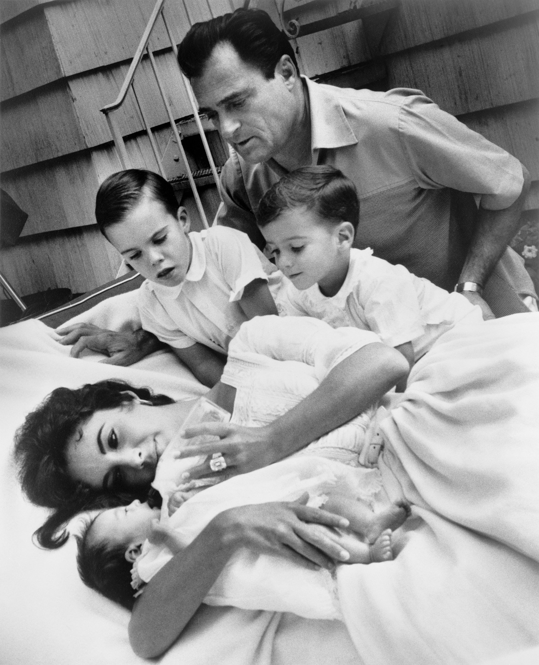 Elizabeth Taylor bottle-feeding newborn Liza Todd with her sons Christopher and Michael H. Wilding, and her husband Michael Todd observing, 1957. | Photograph by Toni Frissell. Wikimedia Commons Images