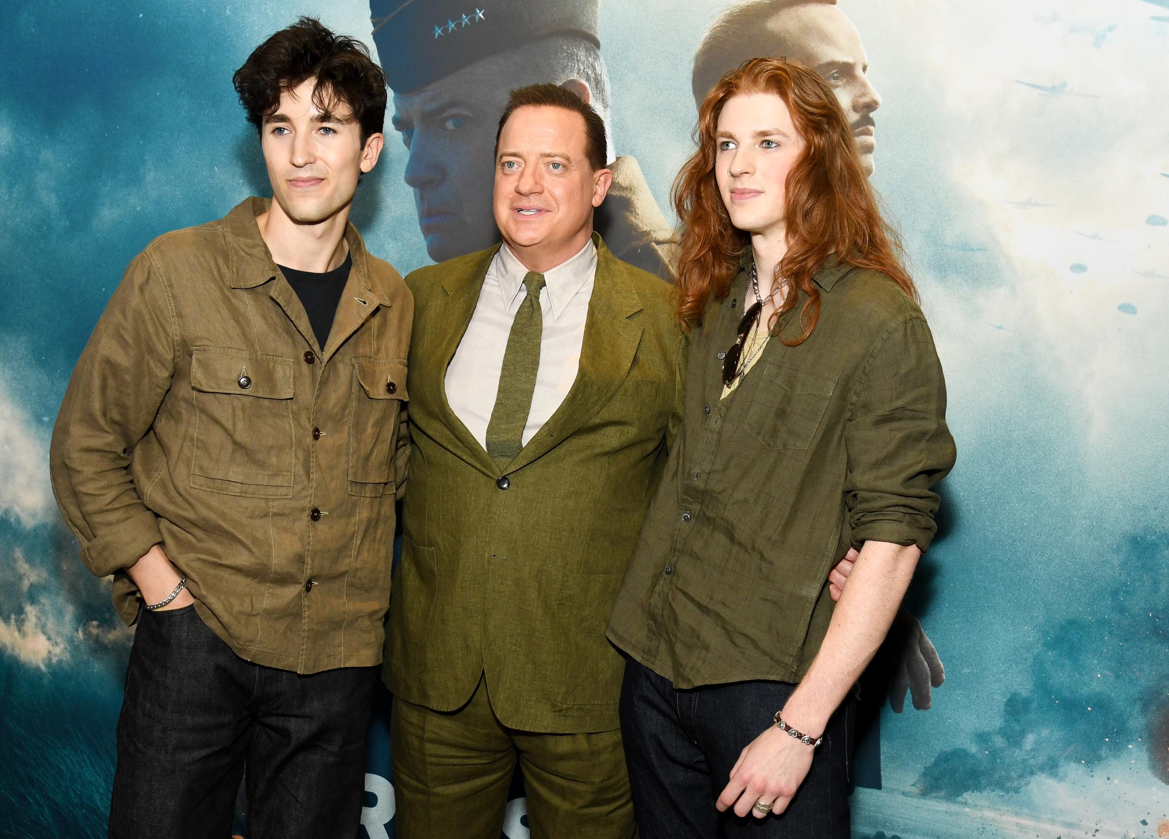 Griffin Arthur Fraser, Brendan Fraser, and Leland Francis Fraser stand arm in arm at the New York premiere of "Pressure," matching the film's blue-toned backdrop in earth-toned outfits.