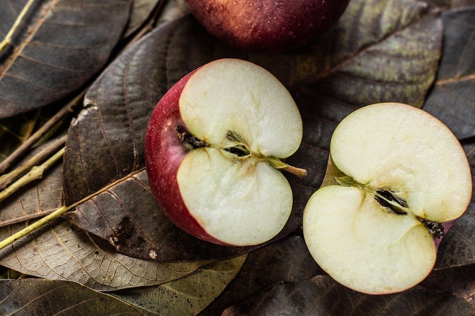Manzana partida a la mitad sobre hojas. | Foto: Pixabay