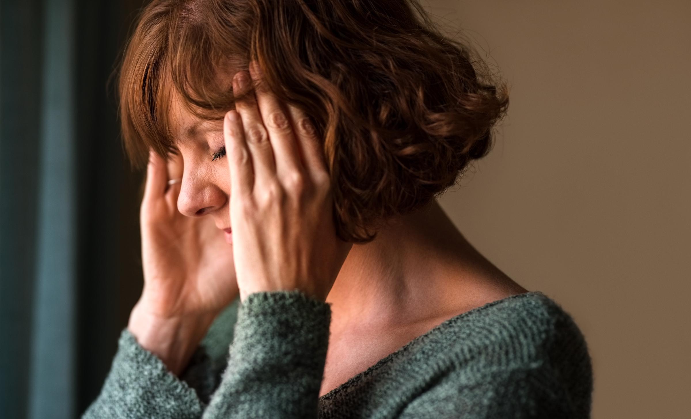 Woman experiencing a headache, rubbing her temples in discomfort | Source: Getty Images