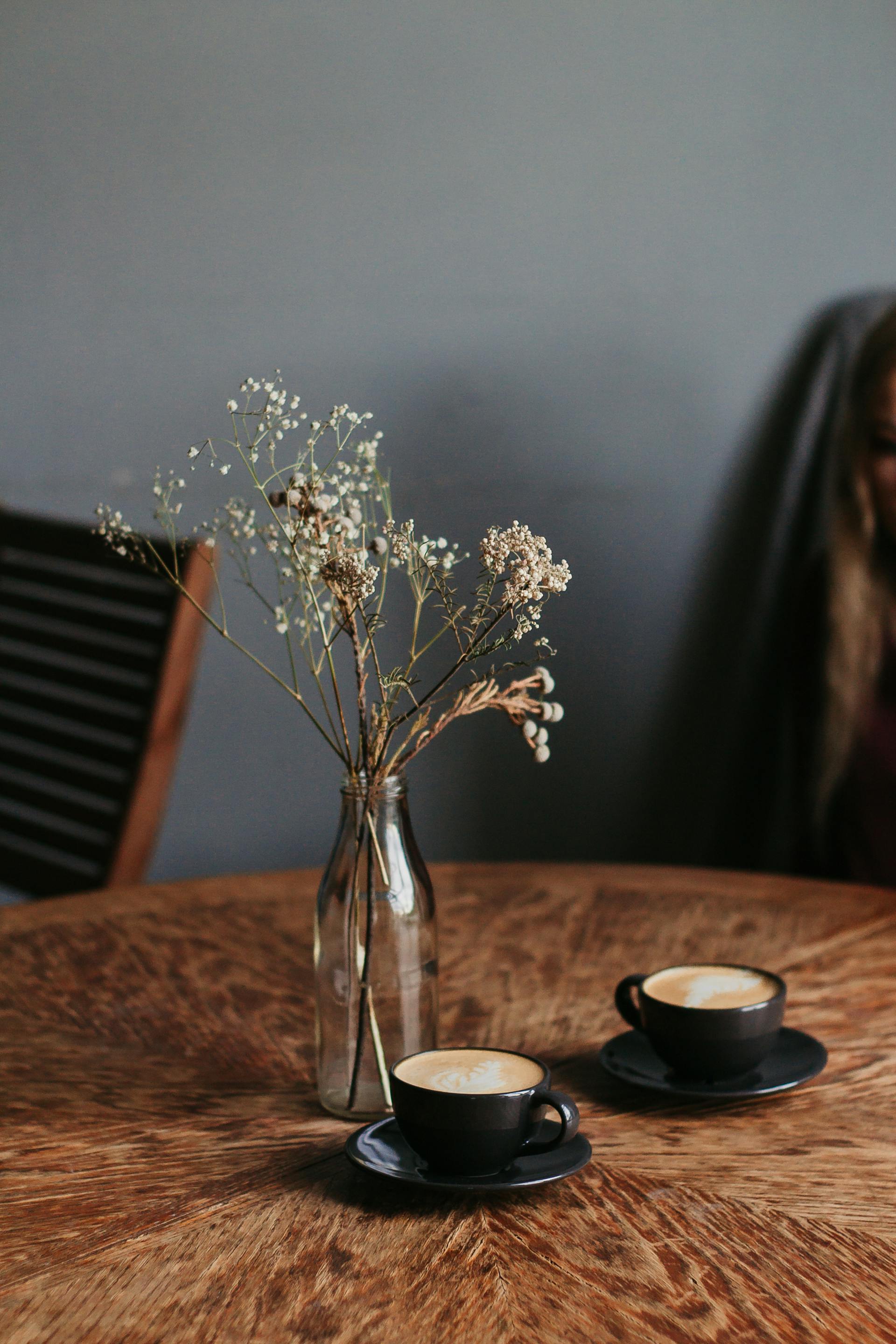 Two cups of coffee near a flower vase on a table | Source: Pexels