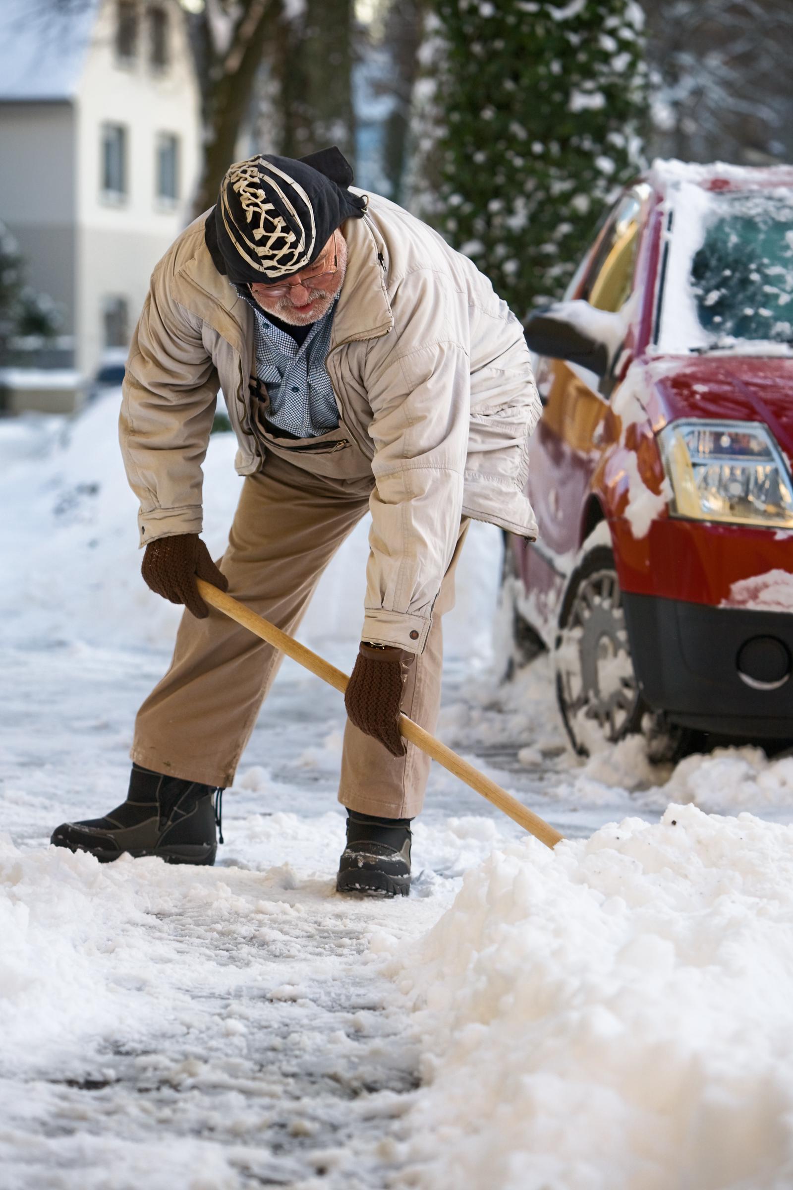 Older man leaning over to lift snow with a shovel | Source: Shutterstock
