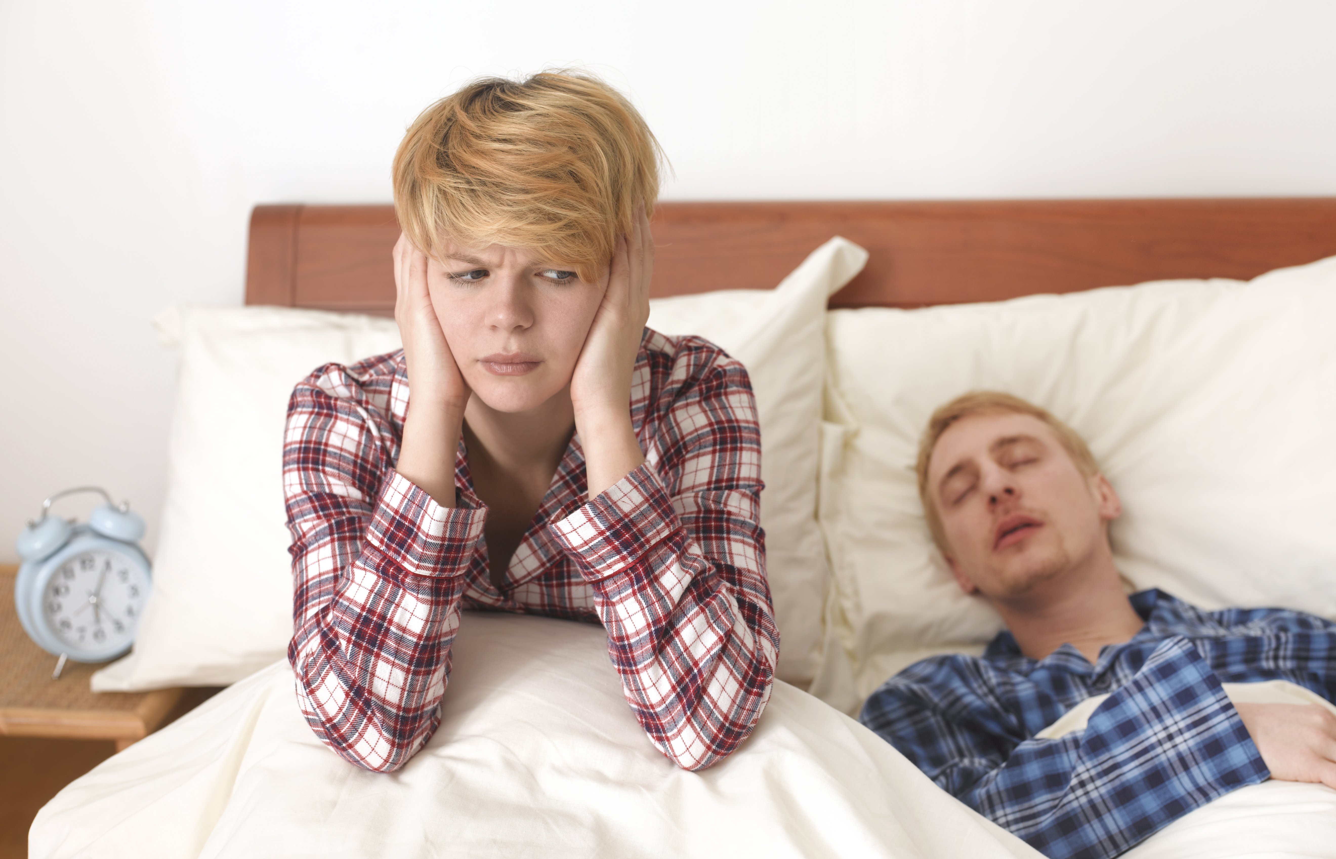 A woman covering her ears as her husband snored beside her. | Photo: Getty images