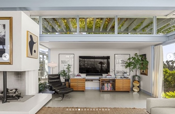 Another angle of the living area reveals the home's mix of midcentury design and contemporary furnishings, including a built-in fireplace, a black lounge chair, and low wooden cabinets. Clerestory windows and glass walls keep the room connected to the outdoors while emphasizing its airy proportions. | Source: Instagram/jparkerstanton