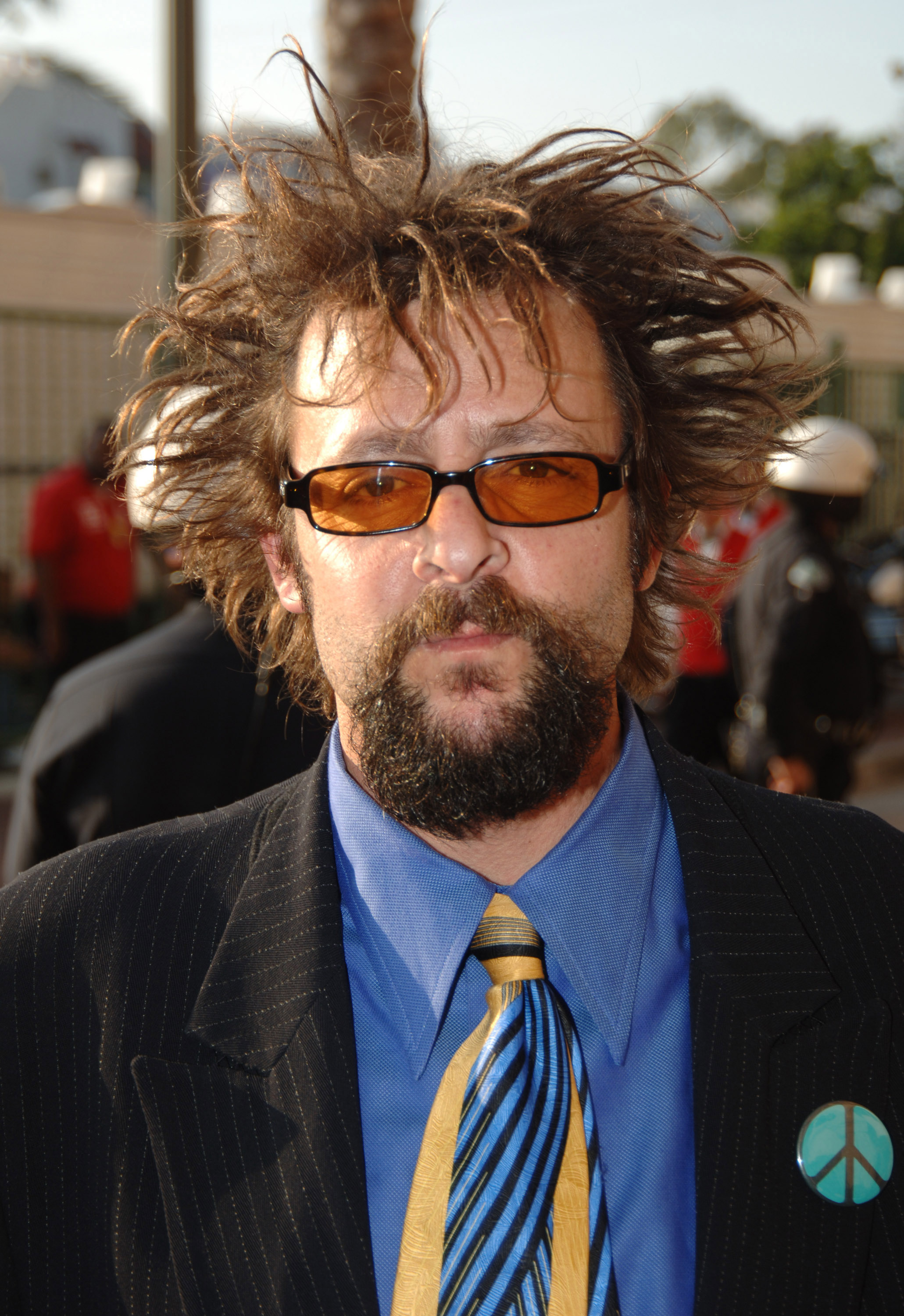 Sporting a distinctive spiky hairstyle, orange-tinted sunglasses, and a peace sign pin on his suit jacket, the star showcased a bold look on the red carpet at the 2005 MTV Movie Awards in Los Angeles. | Source: Getty Images
