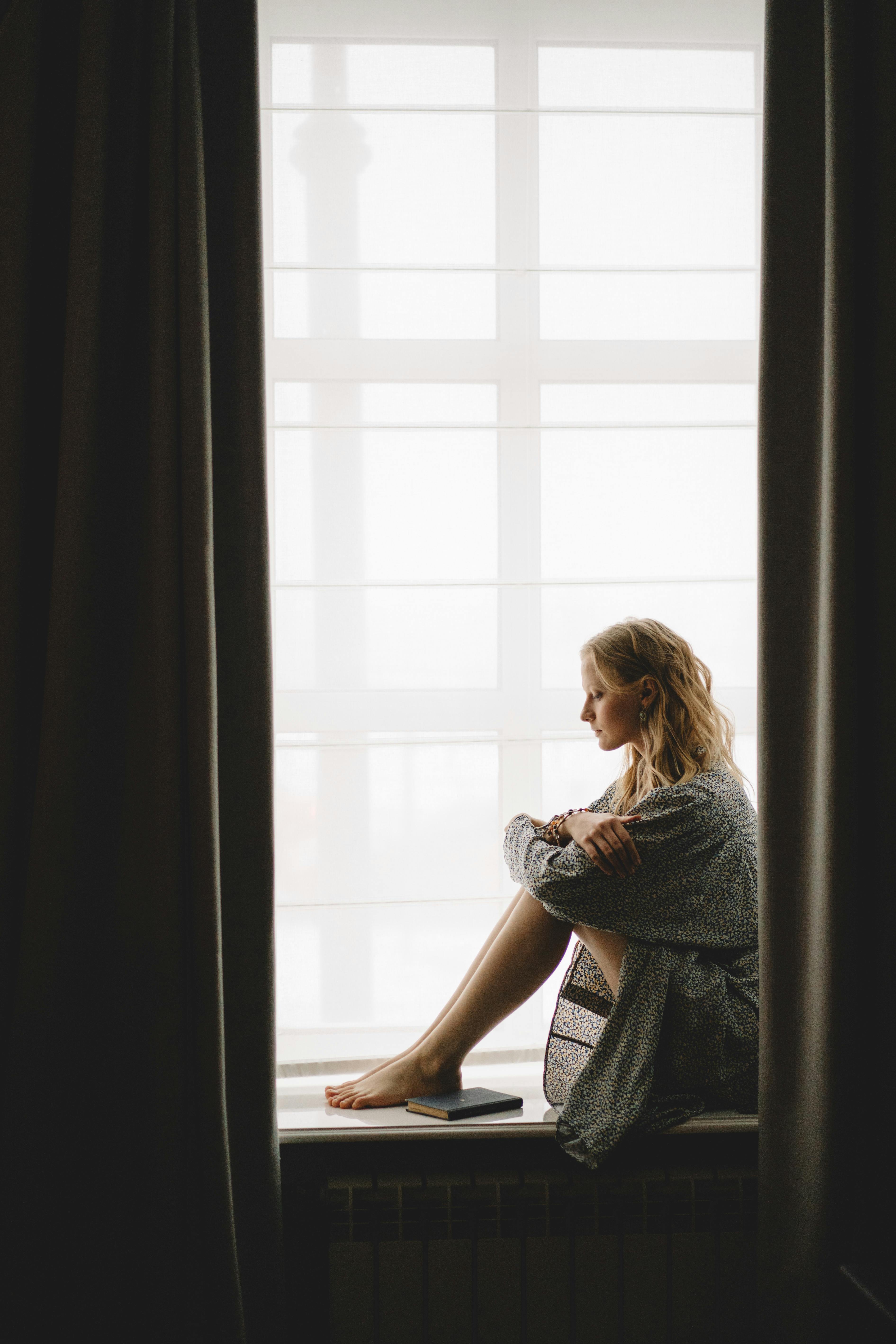 Stressed woman sitting on windowsill | Source: Pexe;s