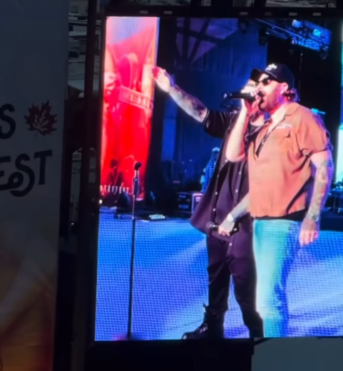 Nate Smith commands the stage with a microphone in hand, performing under bright concert lights in a loose brown shirt, jeans, a black cap, and dark sunglasses. | Source: Instagram/natesmith