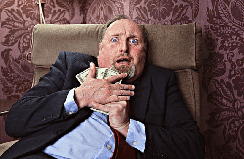 Frightened man sitting on a couch holds onto his money tightly | Source: Getty Images