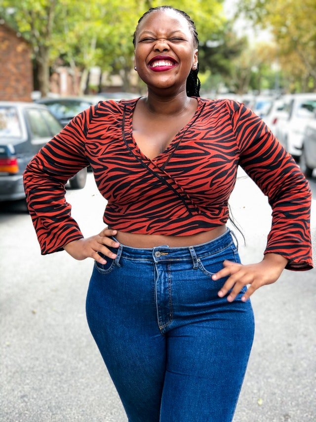 Woman smiles in red top and denim jeans | Photo: Pexels