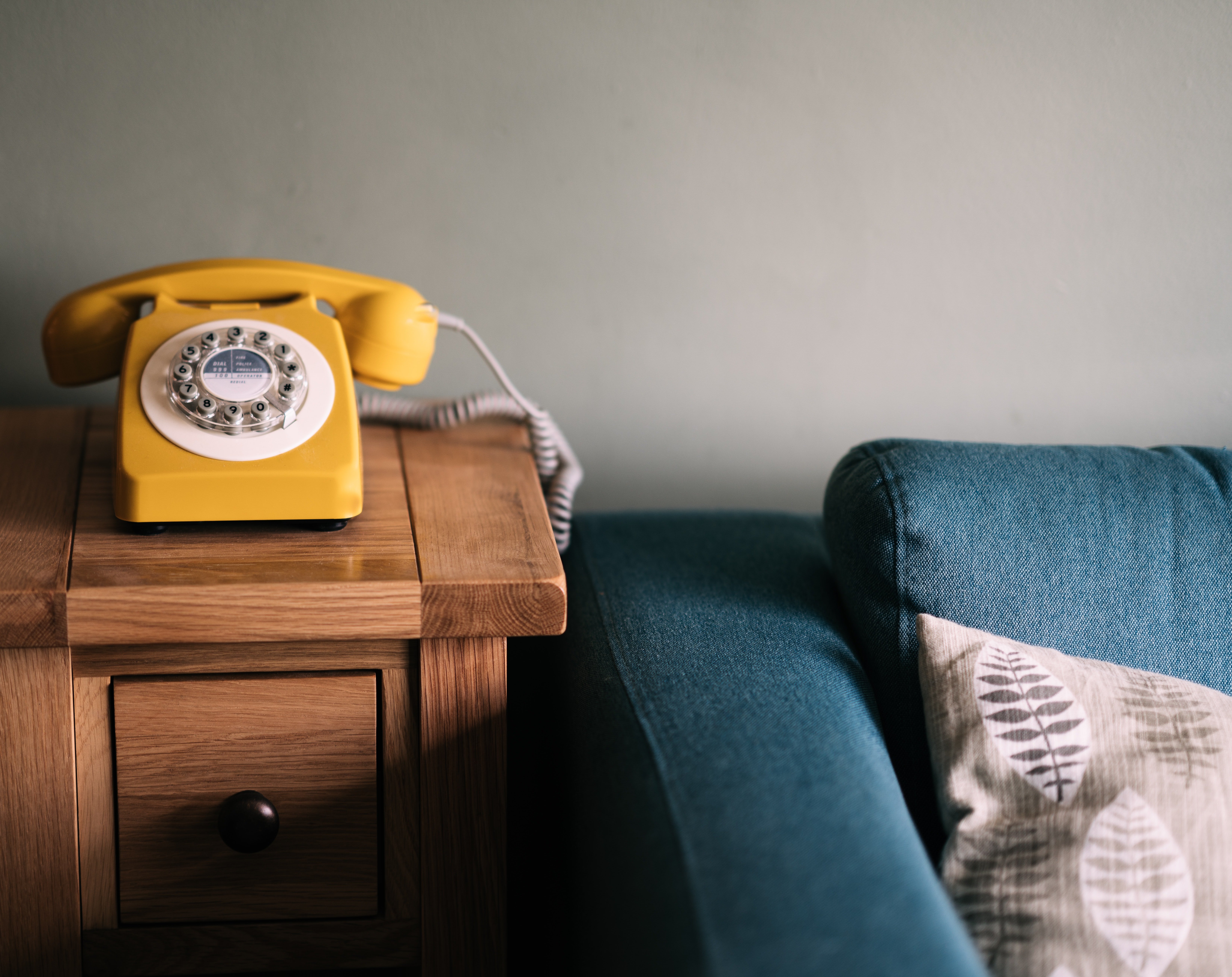 A yellow telephone on a wooden table beside a blue couch. | Source: Unplash