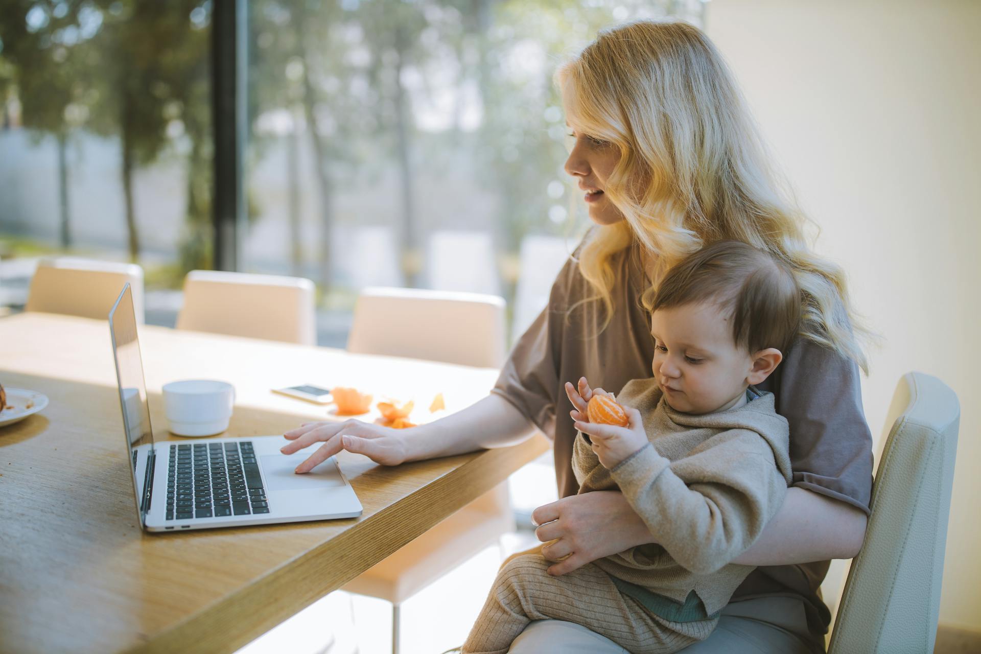 A woman carrying her son while using a laptop | Source: Pexels