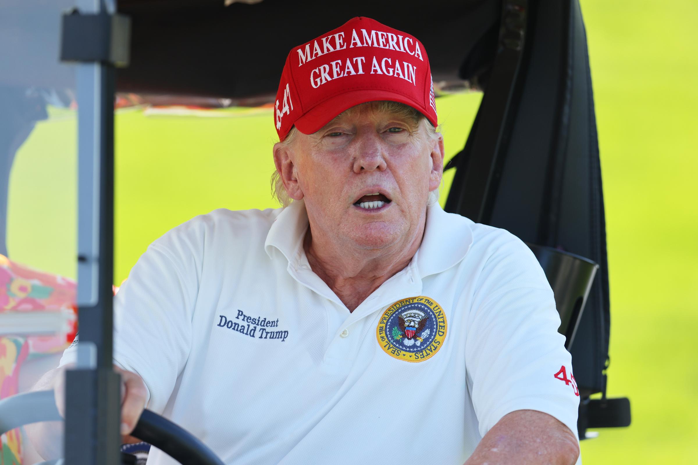 At the Bedminster event in New Jersey on August 11, Donald Trump sits inside a golf cart wearing a white polo with a presidential emblem. His face appears redder than his neck, especially under the bright outdoor light.