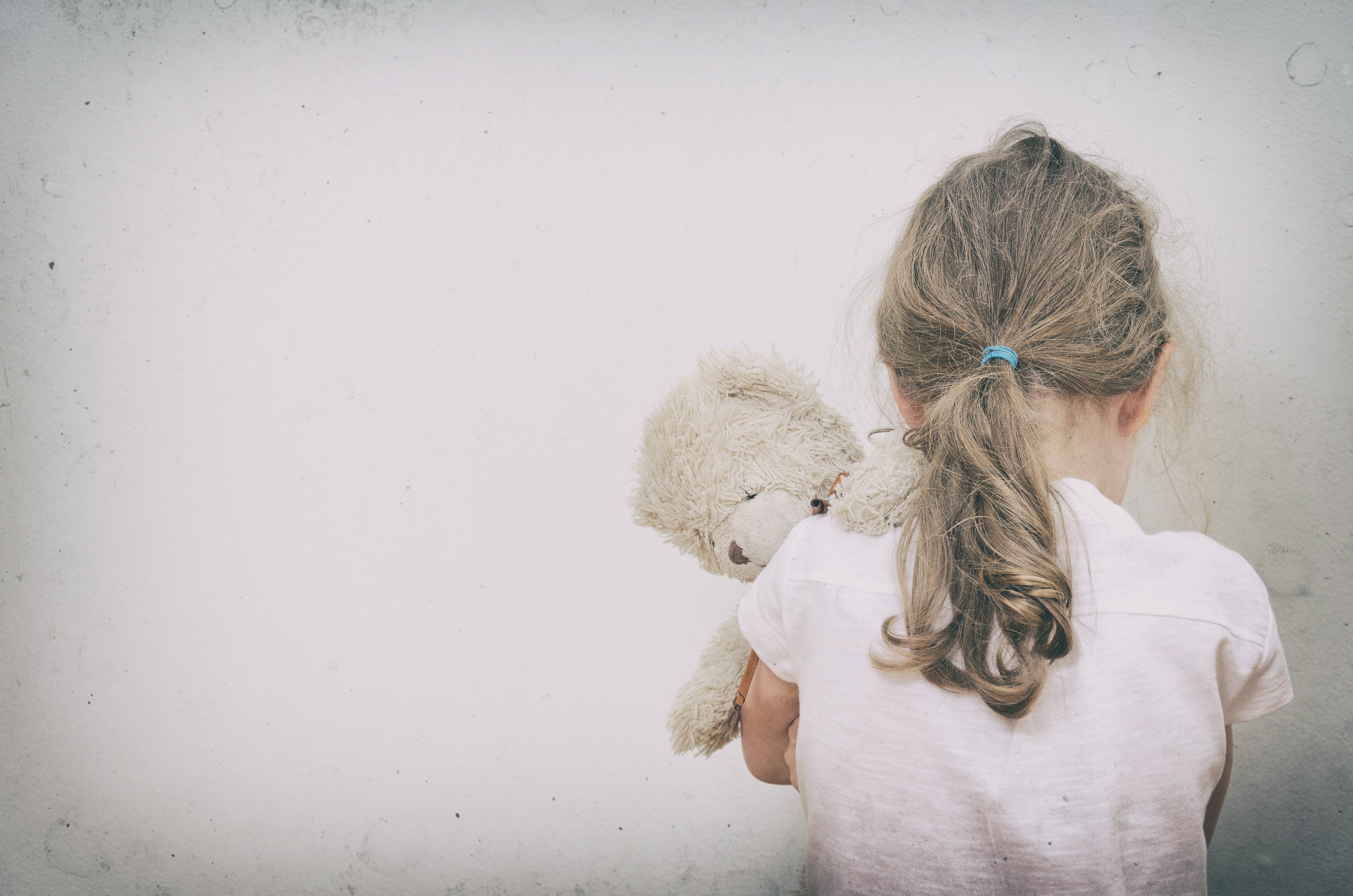 A sad little girl from the back holding her teddy bear. | Source: Shutterstock