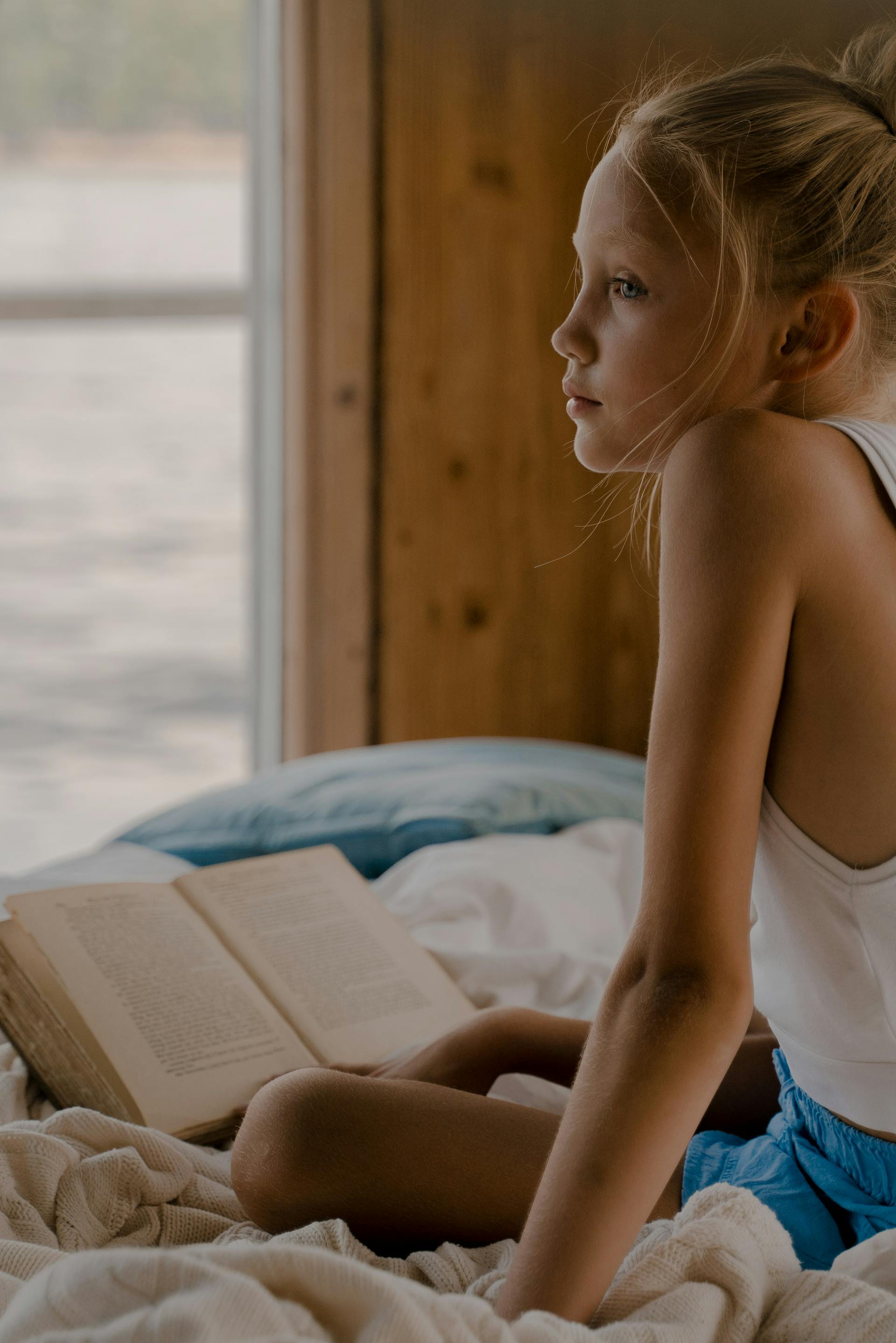 A sad little girl sitting on her bed with a book | Source: Pexels