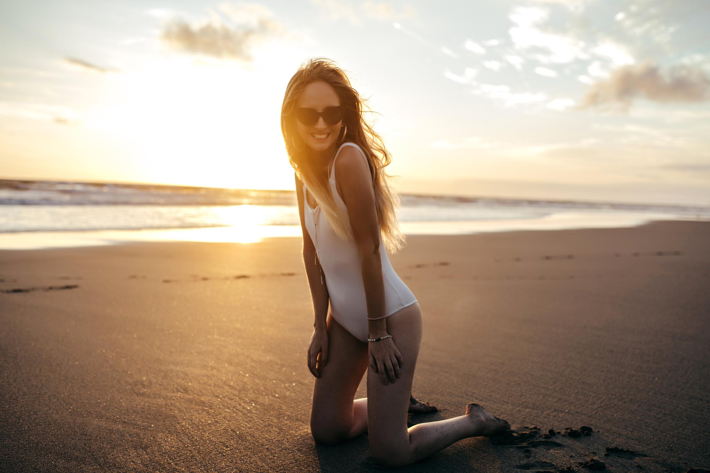 A woman in a white swimsuit kneeling on the beach | Source: Freepik