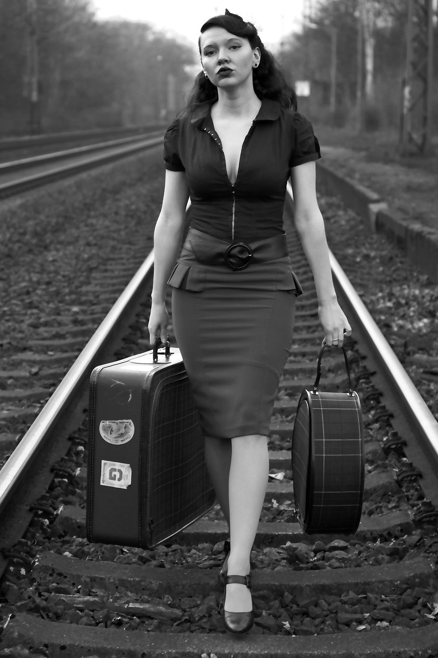 A black-and-white image of a woman carrying bags while walking on railway lines | Photo: Pixabay Juergen_G