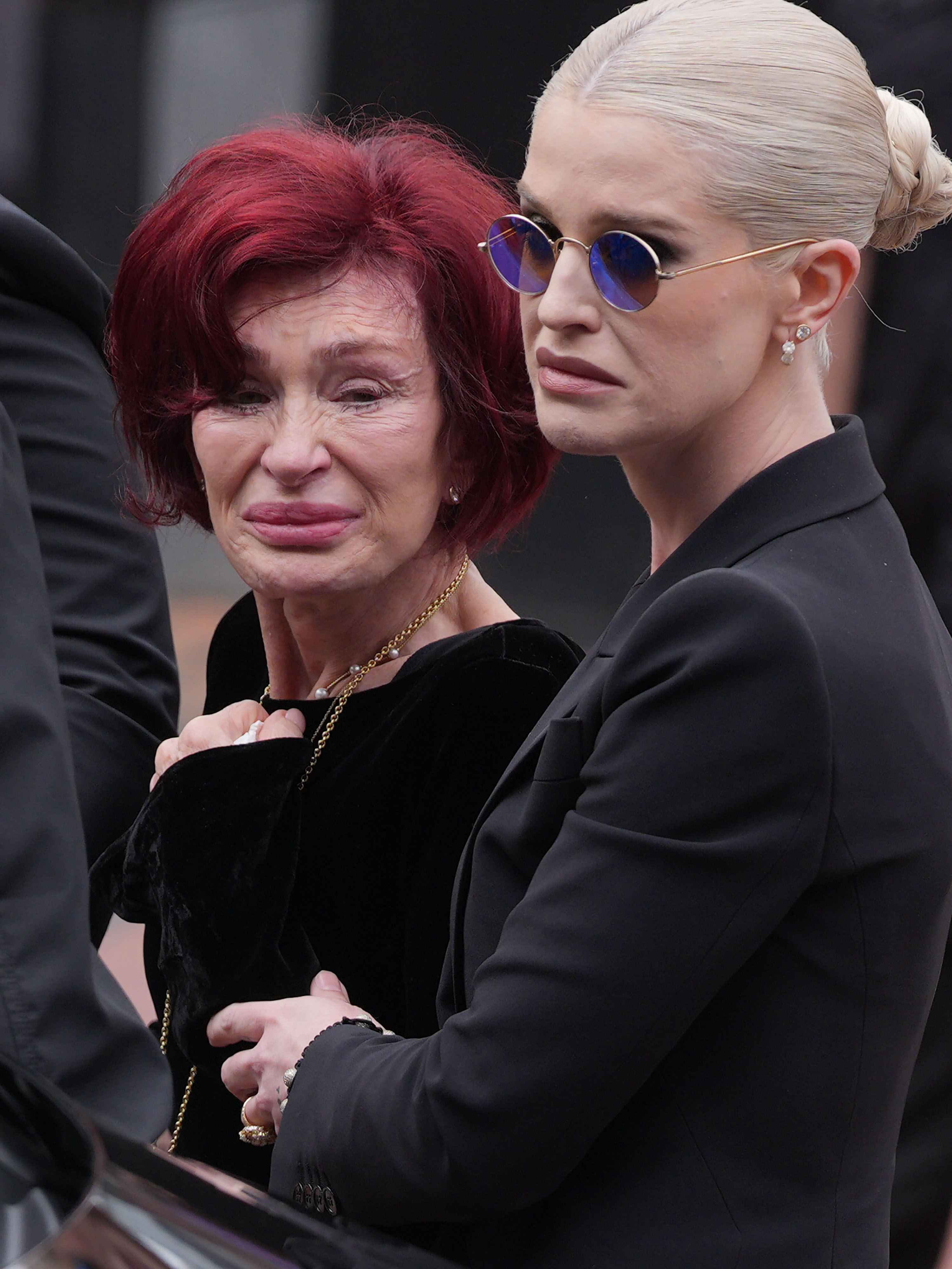 Sharon Osbourne and Kelly Osbourne stop to view tributes to the late Ozzy Osbourne from fans at Black Sabbath Bench and Bridge as his funeral cortege travels through his home city of Birmingham on July 30, 2025 in Birmingham, England. | Source: Getty Images