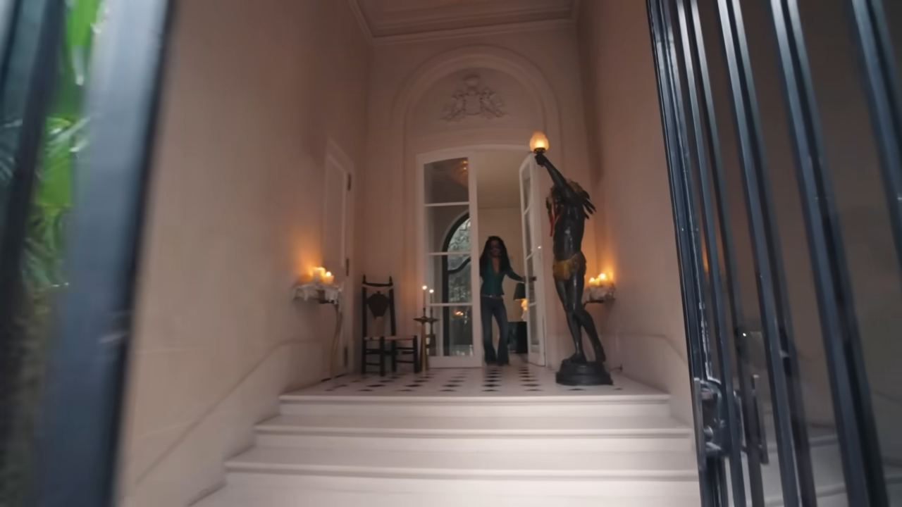 Lenny swings open the front doors to "Hôtel de Roxie," revealing classic checkered tile floors and a dramatic black statue holding a glowing torch. | Source: YouTube/@Archdigest