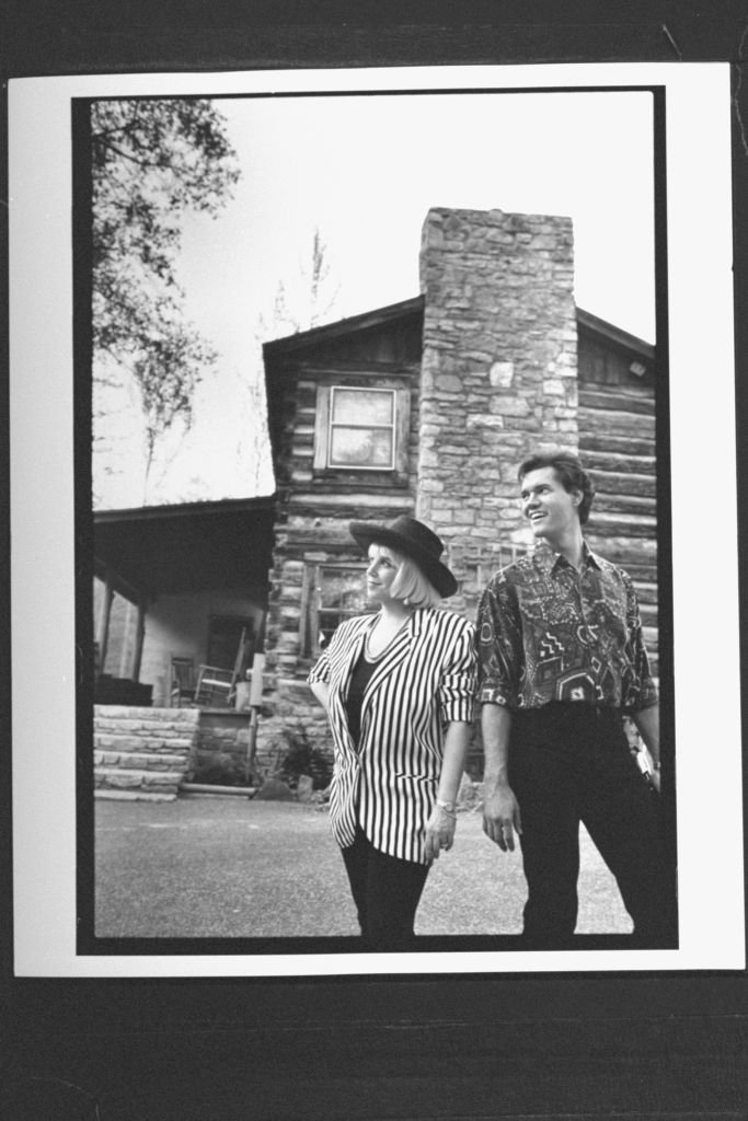 Randy Travis and Lib Hatcher posing in front of the entrance to their log cabin circa 1991 | Photo: Getty Images
