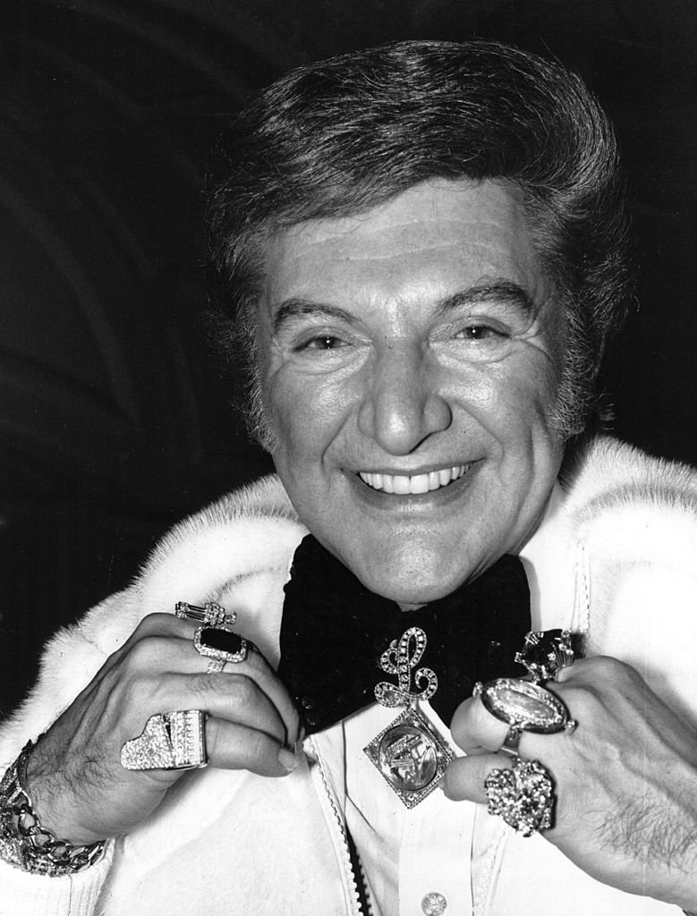 American pianist Liberace (1919 - 1987) displays his wealth of jewellery as he sweeps into London Airport. | Getty Images