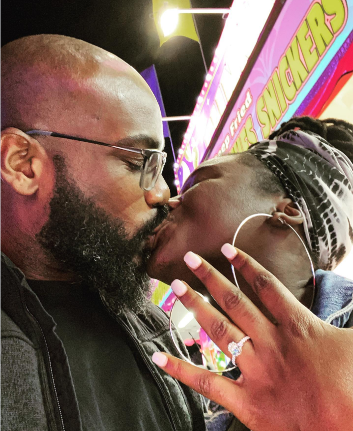 Nancy Metayer Bowen and her husband, Stephen Bowen, share a close, affectionate moment as they kiss, with her hand raised in the foreground to reveal a sparkling engagement ring, set against a colorful, brightly lit backdrop that suggests a lively night out. | Source: Instagram/kingsb85