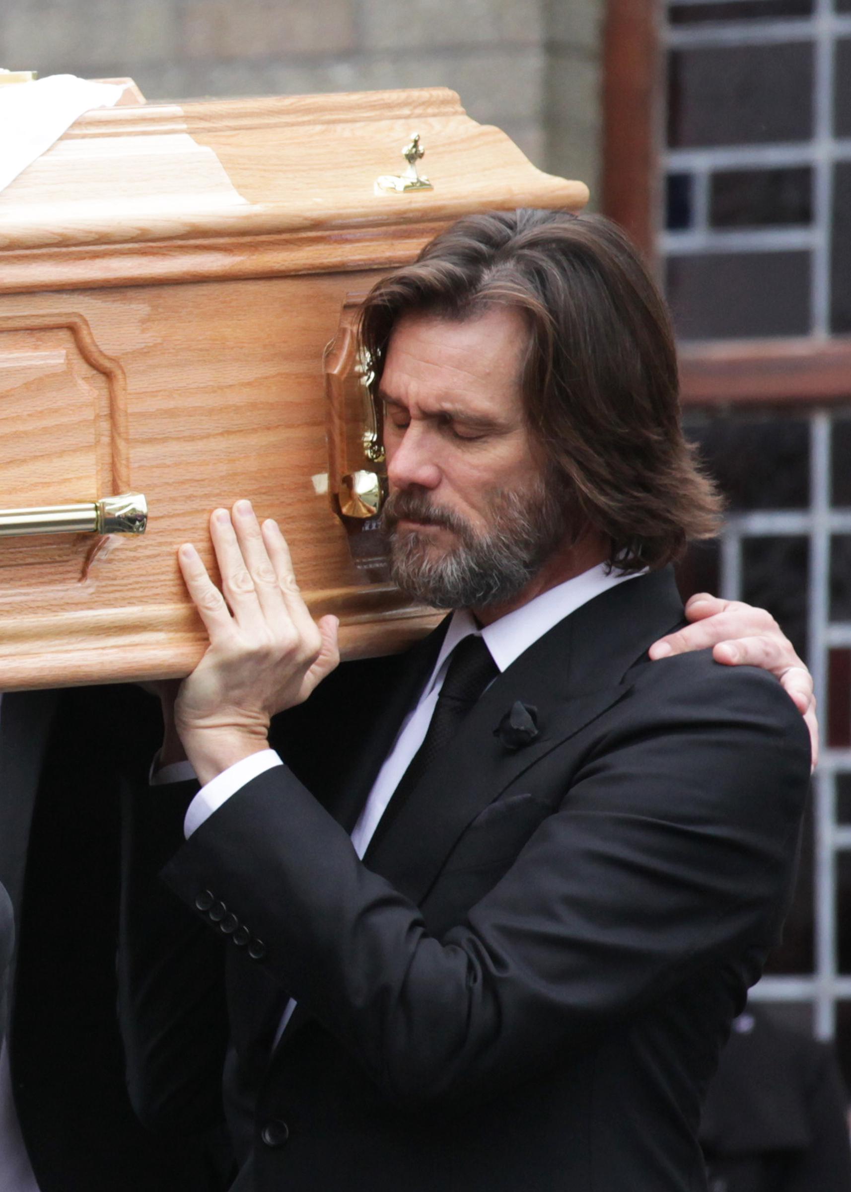 In this photo, Jim Carrey solemnly carries the casket at the funeral of his ex-girlfriend Cathriona White. Dressed in a black suit and tie, he appears deeply emotional, his eyes closed in grief and respect. The somber moment reflects his mourning and quiet strength during the heartbreaking occasion.