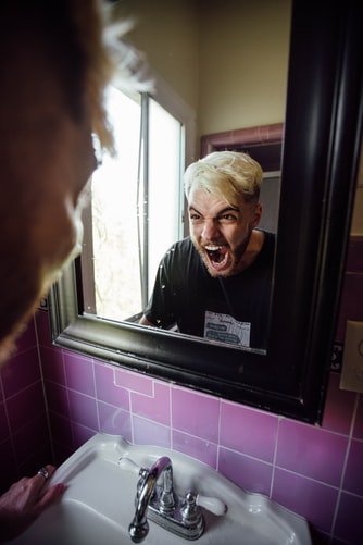 An angry man stares at himself in a bathroom mirror | Photo: Unsplash