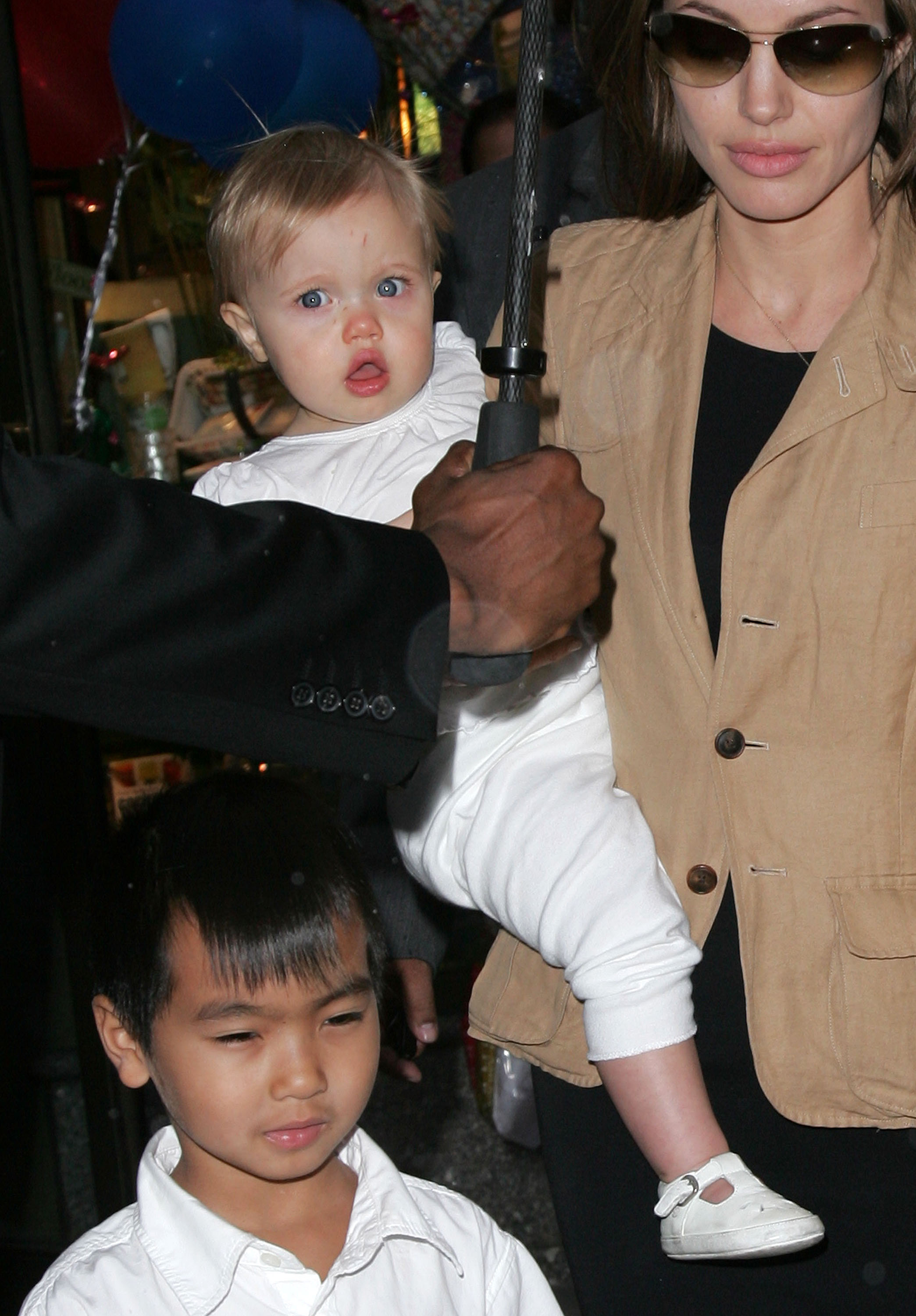 Angelina Jolie carries baby Shiloh Jolie-Pitt while out in New York City with Maddox. Dressed in white, Shiloh looks wide-eyed and curious as she takes in her surroundings. The candid moment captures one of her earliest public appearances.