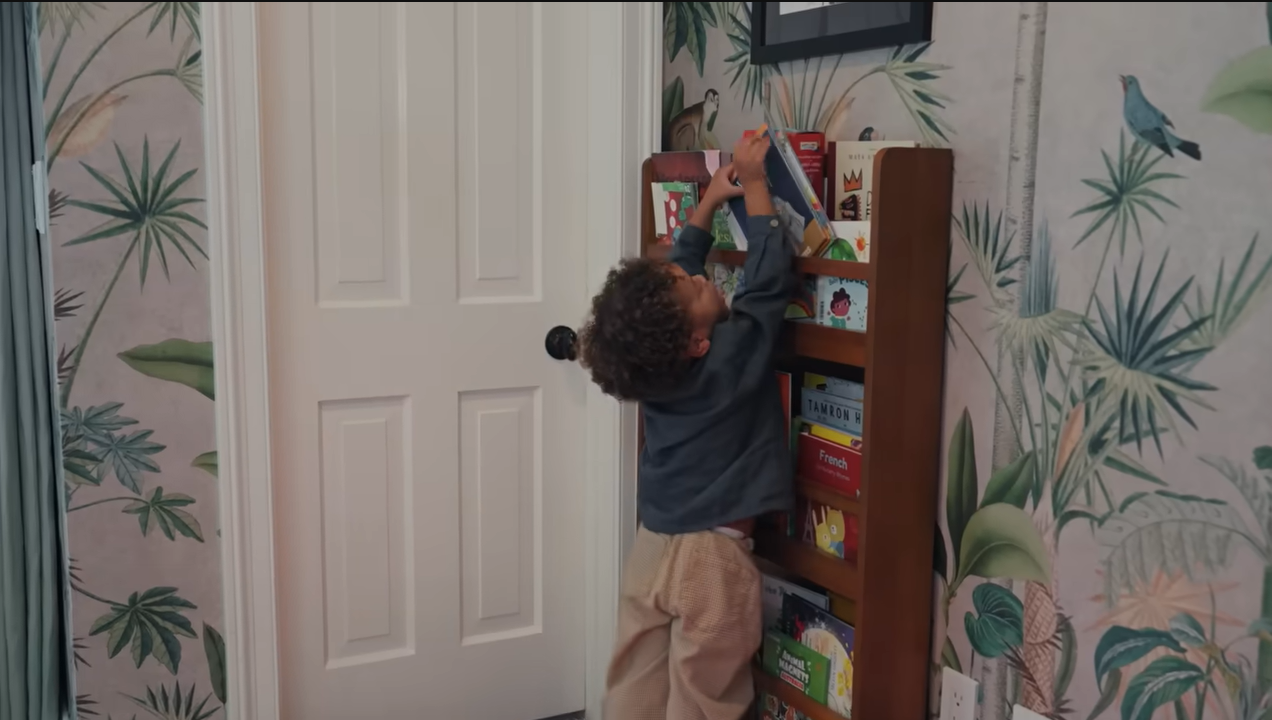 Little Leo stretches up high to pull a book off his custom wooden shelves. | Source: YouTube/@Archdigest