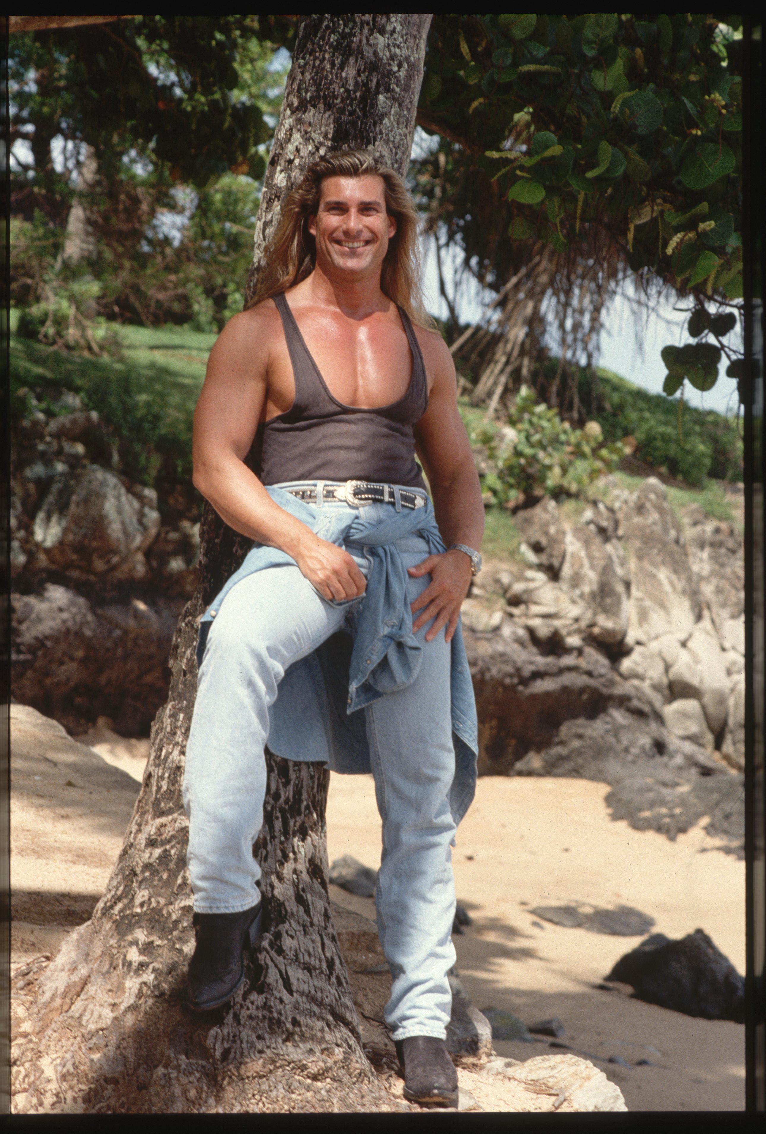 Fabio Lanzoni is pictured wearing a tank top and jeans leaning against a tree in Hawaii (date not specified) |  Source: Getty Images
