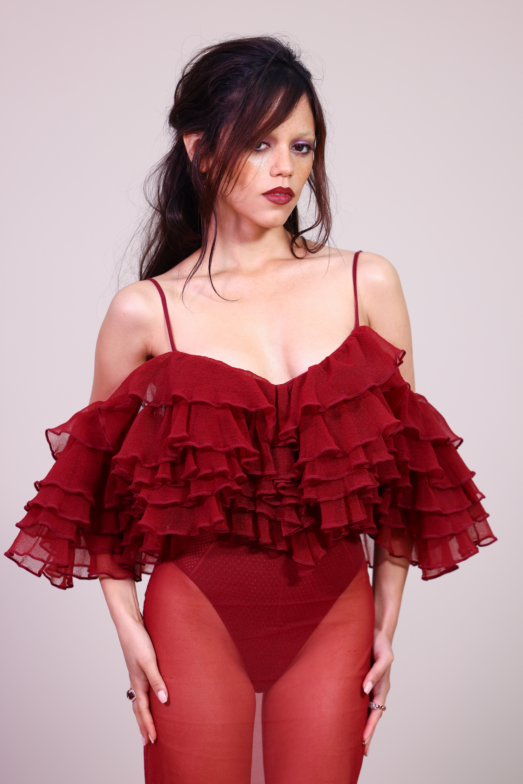 Jenna Ortega attended the Givenchy Women’s Spring/Summer 2026 show at Paris Fashion Week in France. She wore a red, floor-length dress featuring a tiered, ruffled off-the-shoulder bodice with spaghetti straps. It is styled with a sheer skirt layered over high-cut briefs.