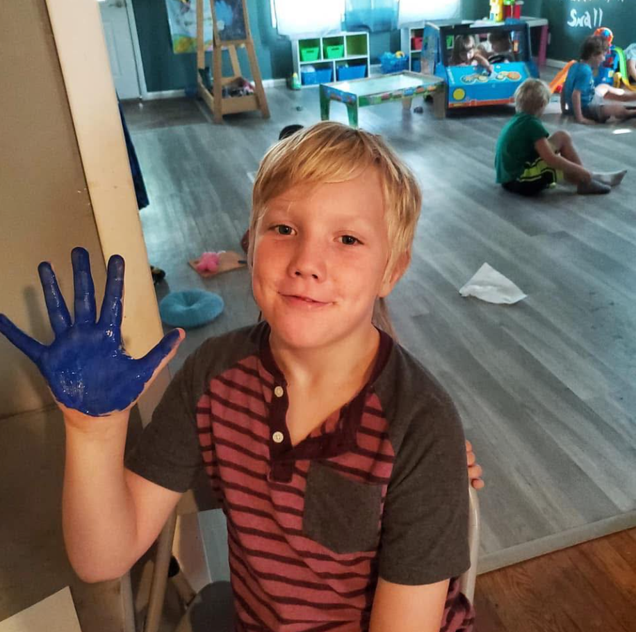 Caleb Moore is photographed with blue paint on his palm and a smile on his face, from a post dated June 12, 2025 | Source: Facebook/AshleyBentz
