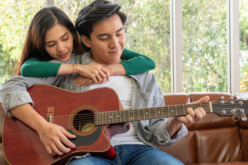 Mujer abraza a su novio mientras él toca la guitarra. | Foto: Shuttertock Mujer abraza a su novio mientras él toca la guitarra. | Foto: Shuttertock
