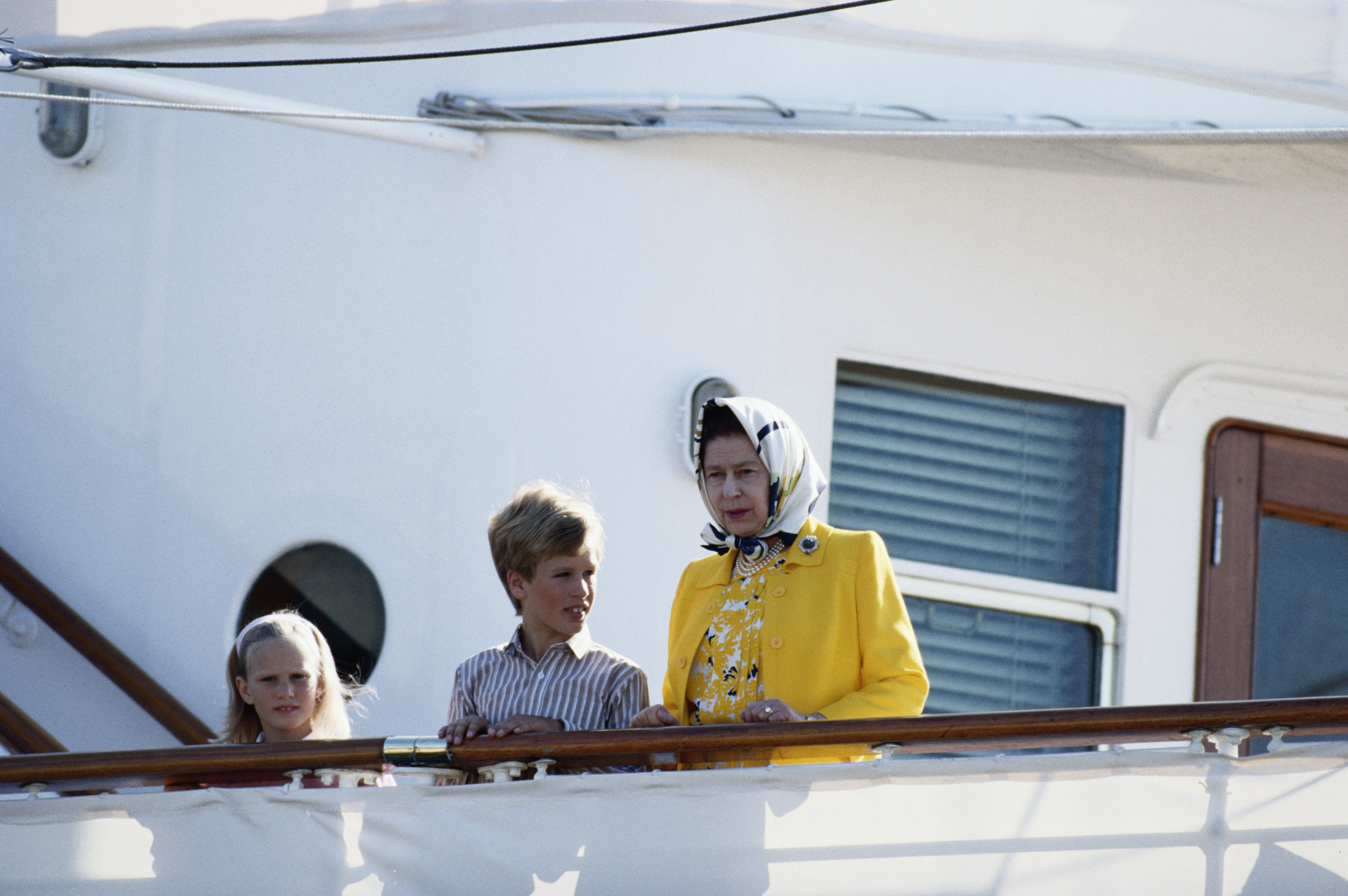 Zara Phillips mit ihrem Bruder Peter Philips und ihrer Großmutter Königin Elizabeth II. an Bord der königlichen Yacht "Britannia" zu Beginn einer Kreuzfahrt zu den westlichen Inseln, Großbritannien, 5. August 1988 | Quelle: Getty Images