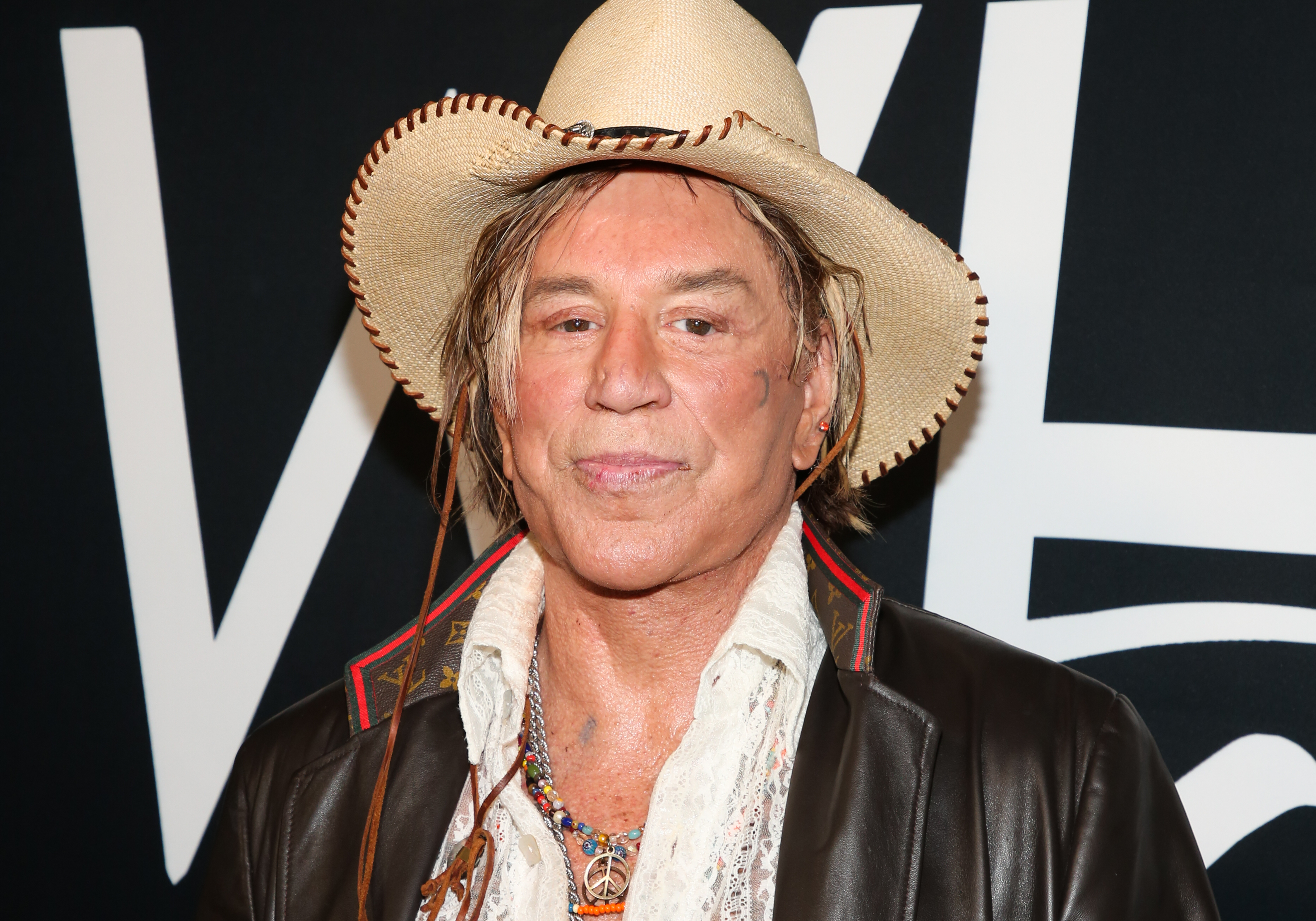 Mickey Rourke embraced a Western-inspired look for the TEATRO Even Summer White Affair at Skybar in West Hollywood, California, on June 17, 2022. Wearing a wide-brimmed cowboy hat over tousled hair, the actor paired a dark leather jacket and lace shirt with layered, colorful necklaces as he posed for a close-up at the event.