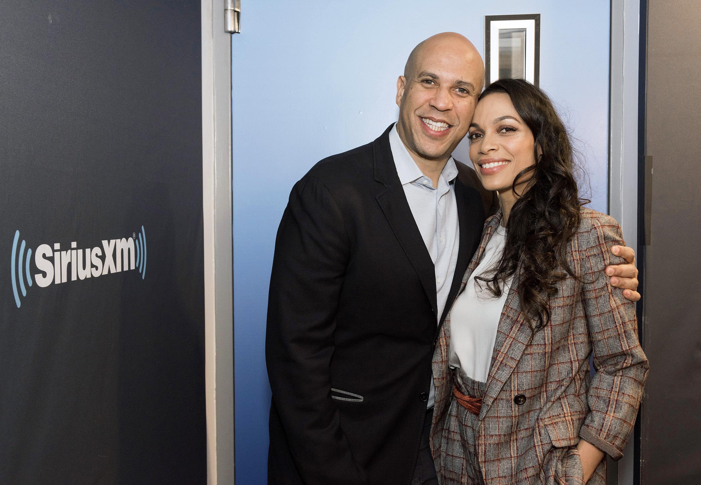 During an exclusive visit to SiriusXM Studios in New York City, Cory Booker and Rosario Dawson share a warm, relaxed moment, smiling effortlessly as they pose for the camera.