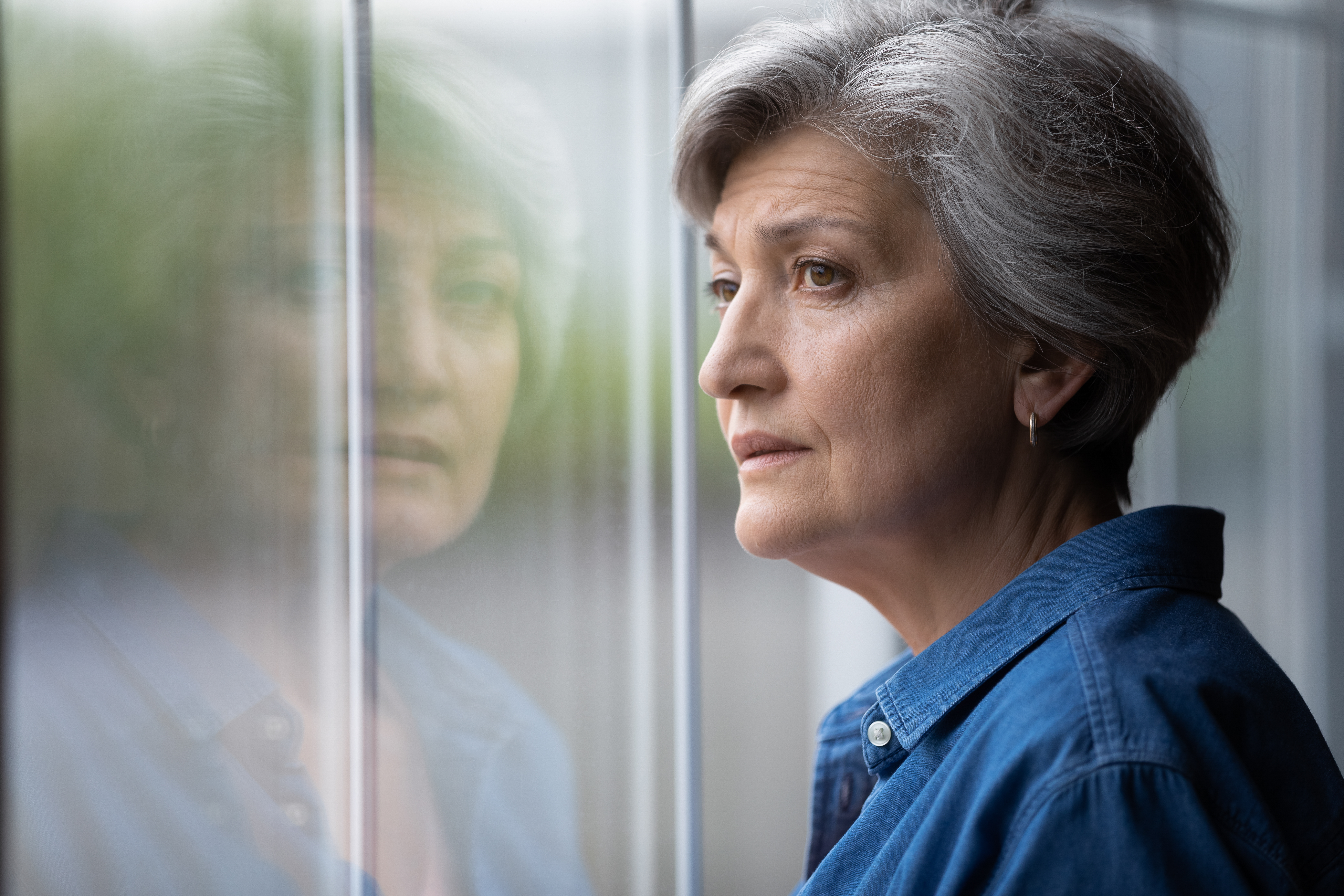 An anxious senior lady looking through the window | Source: Shutterstock
