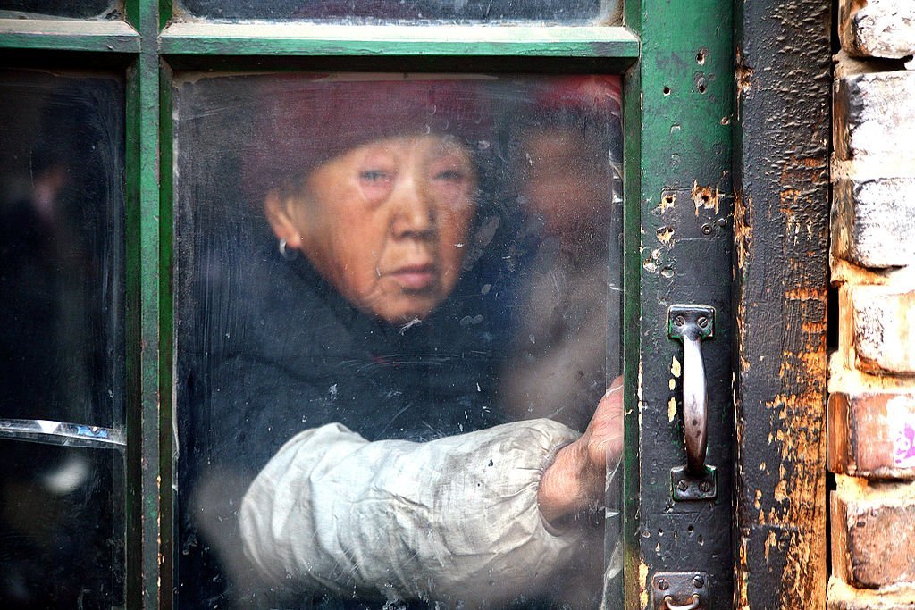 An old woman holds onto the windowpane as she looked out, on December 27, 2008 | Source: Getty Images