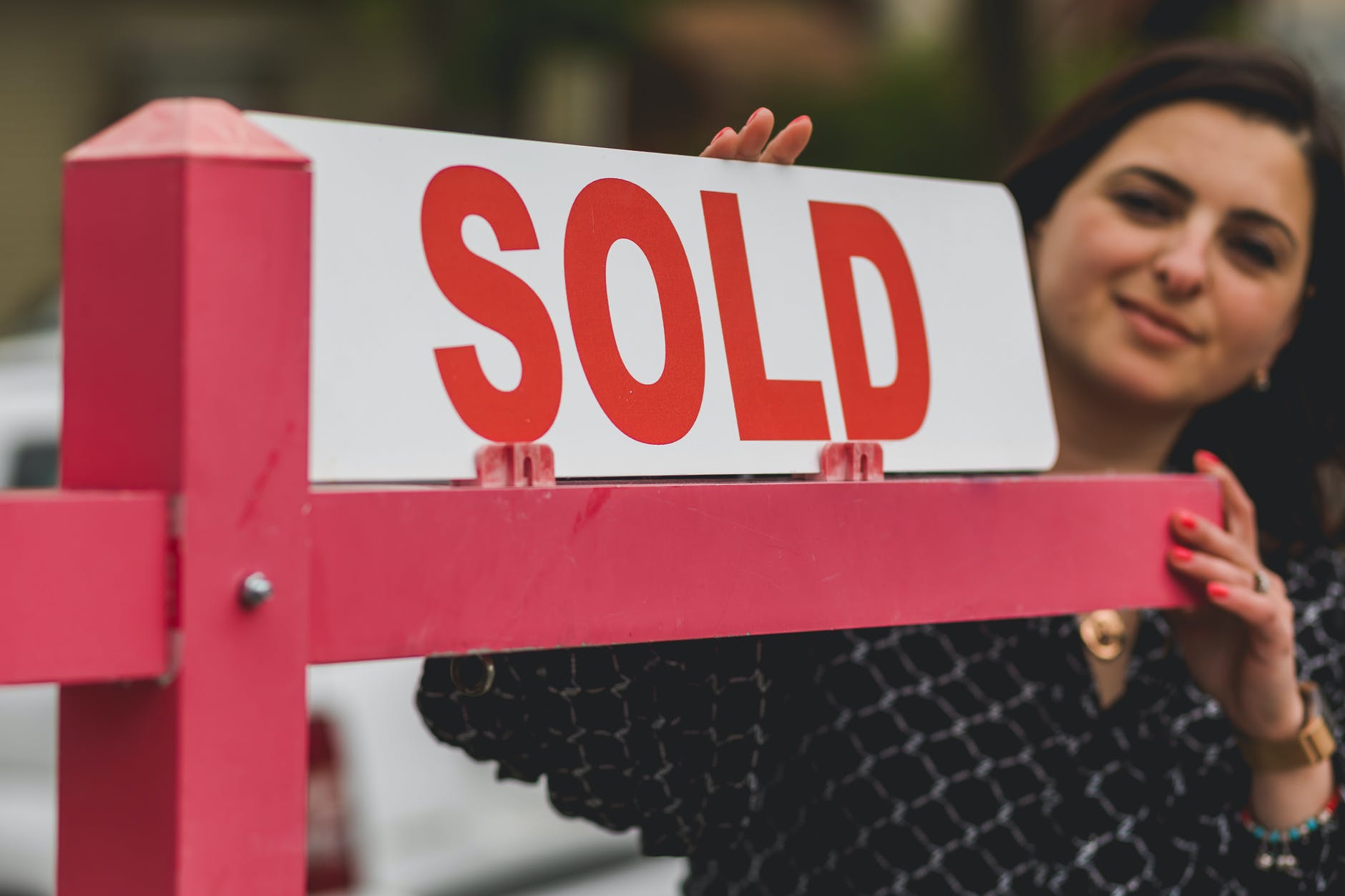 Mujer junto a un cartel con la palabra "vendida" frente a una vivienda. | Foto: Pexels