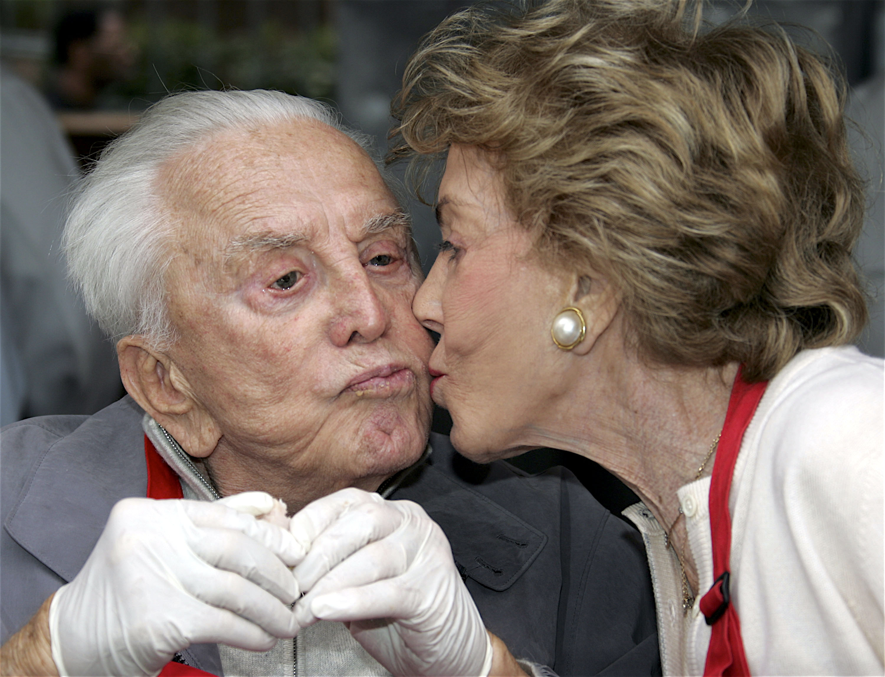 Actor Kirk Douglas receiving a kiss from his wife, Anne Buydens, between serving meals at the Los Angeles Mission and Anne Douglas Center's Thanksgiving Meal for the Homeless on November 23, 2005 in Los Angeles, California | Source: Getty Images