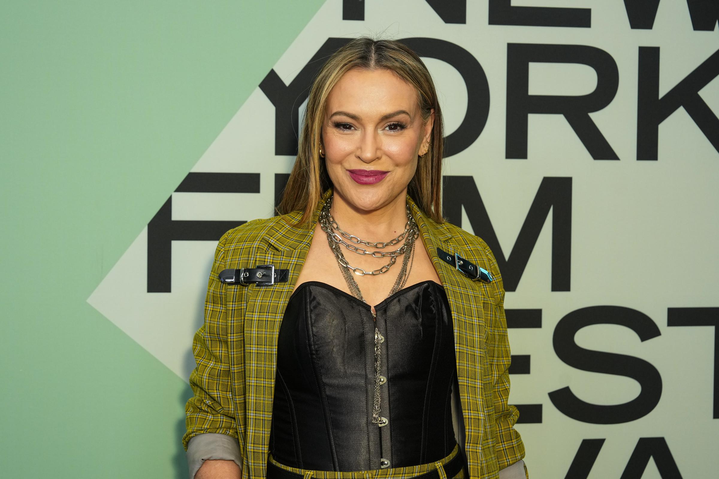 Alyssa Milano attends the 2025 New York Film Festival wearing a bold yellow plaid ensemble paired with a black corset top. Layered silver chains and statement clasps on her jacket add an edgy, fashion-forward touch. Her sleek, straight hair and vibrant lipstick complete the confident red carpet look.