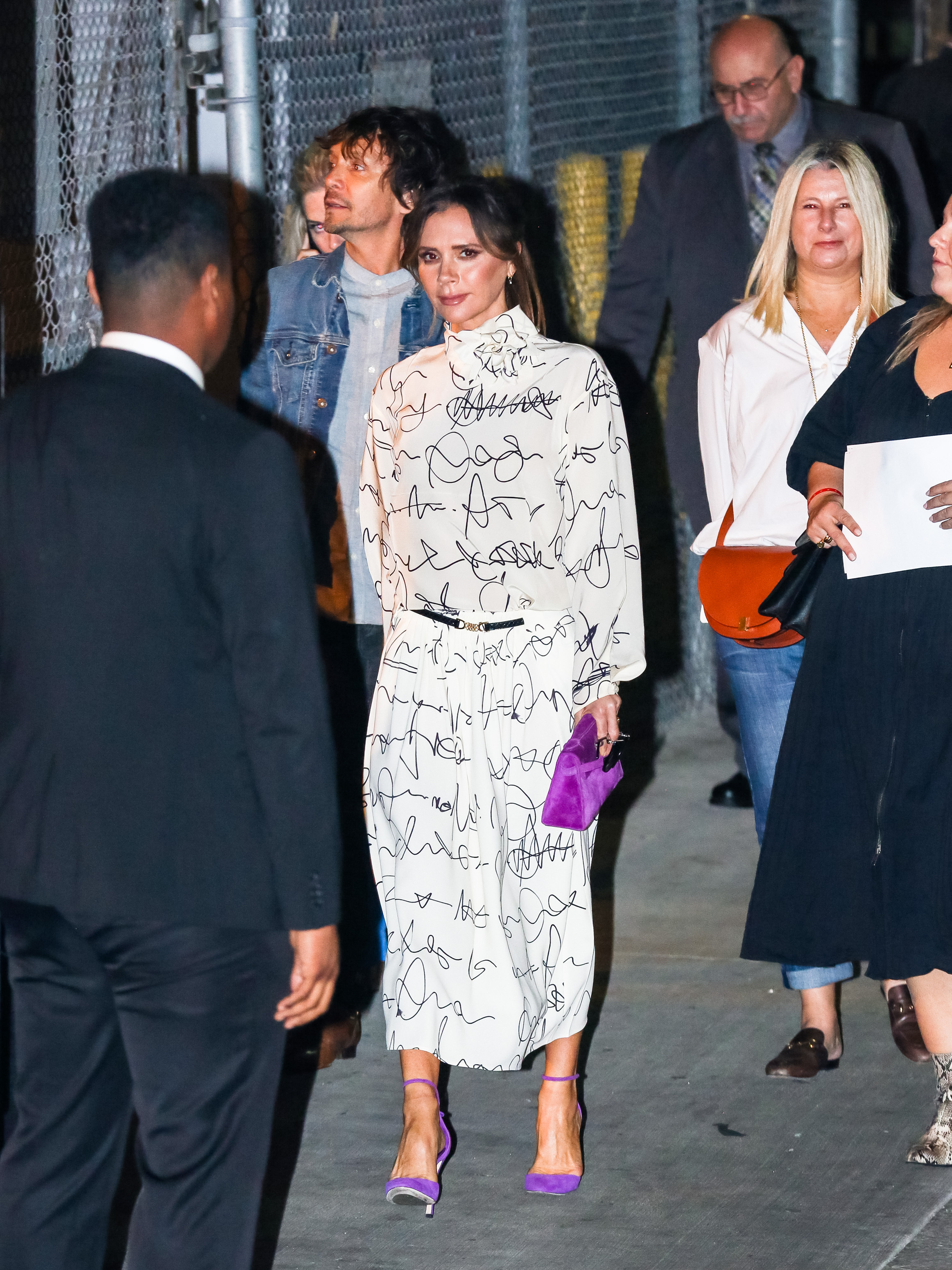 On 19 November 2019, Beckham arrives at "Jimmy Kimmel Live" in Los Angeles, turning heads in a fluid printed dress and bold purple heels. With a matching clutch and effortless polish, she offers a masterclass in elevated day-to-night dressing.