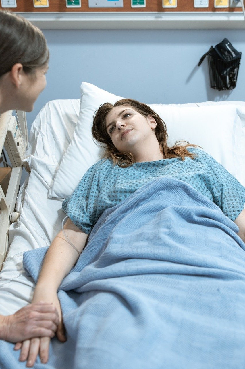 Una joven mujer habla con otra que descansa en una cama de hospital. | Foto: Shutterstock