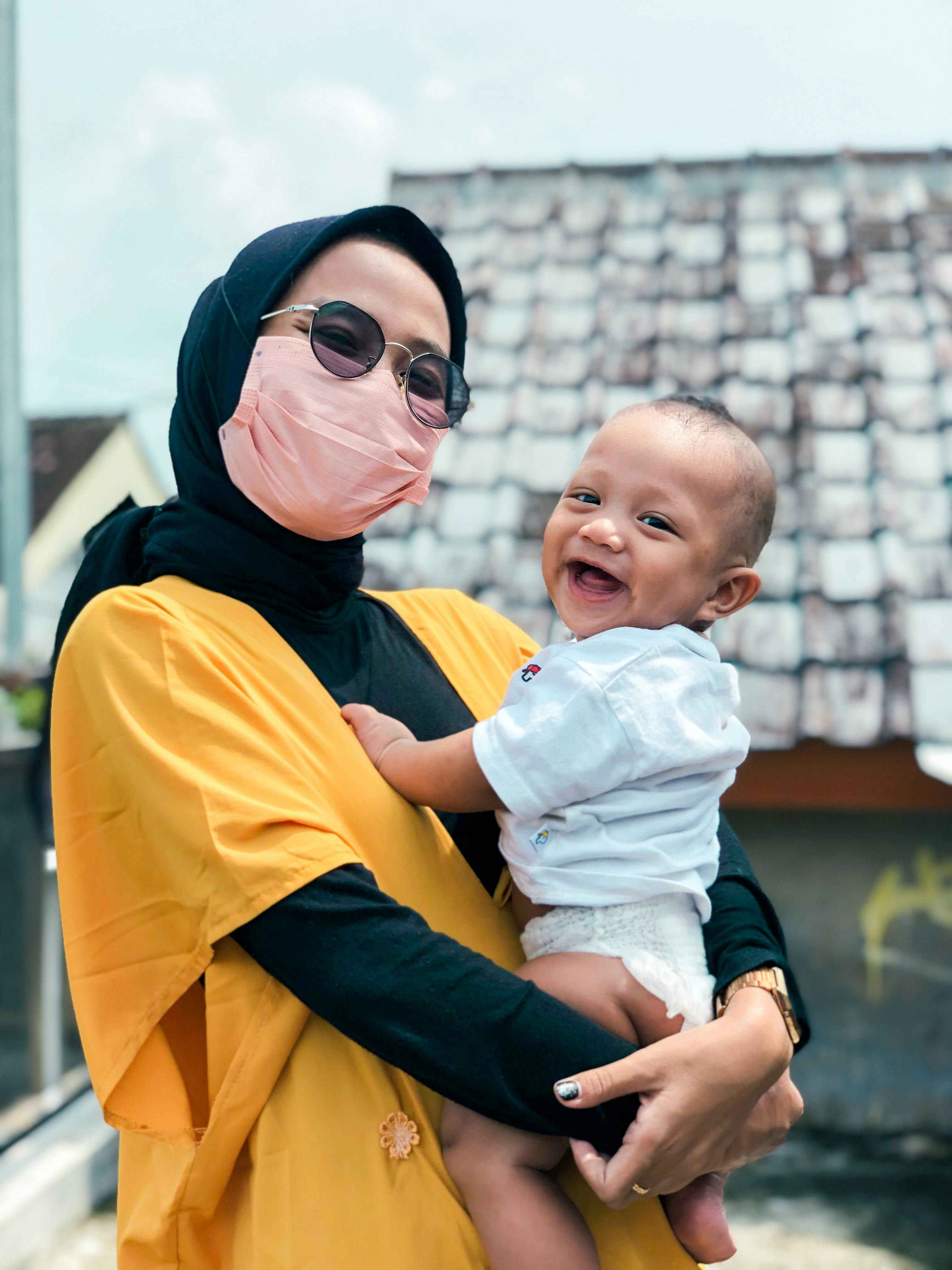 A woman wearing a mask and holding a smiling baby | Source: Pexels