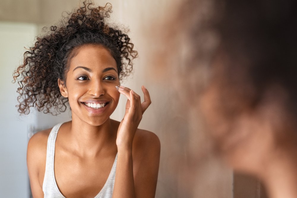 A photo of a young black woman applying cream on her face. | Photo: Shutterstock.
