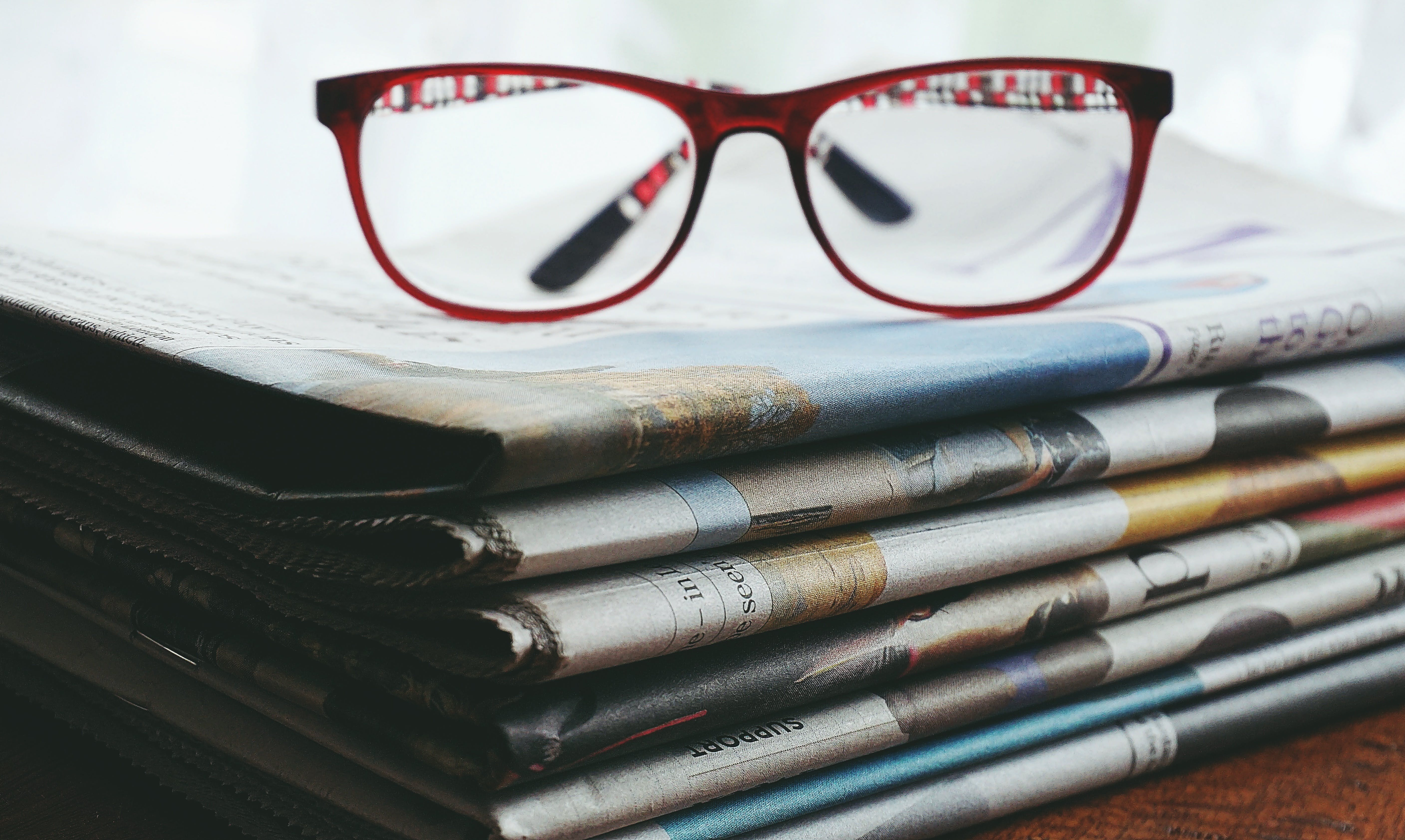 Red framed eye glasses on newspapers. | Source: Pexels